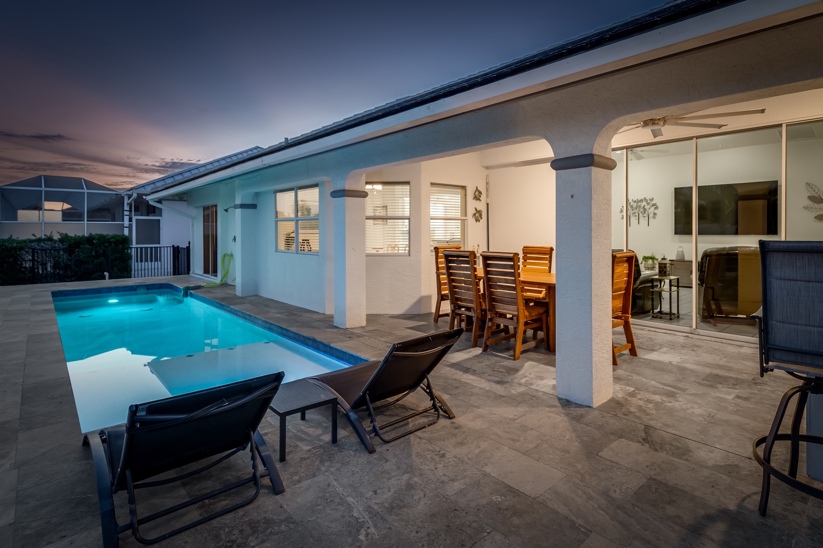 A private oasis unfolds at twilight, where the illuminated pool beckons beside covered patio seating perfect for alfresco dining or peaceful evenings under the stars.