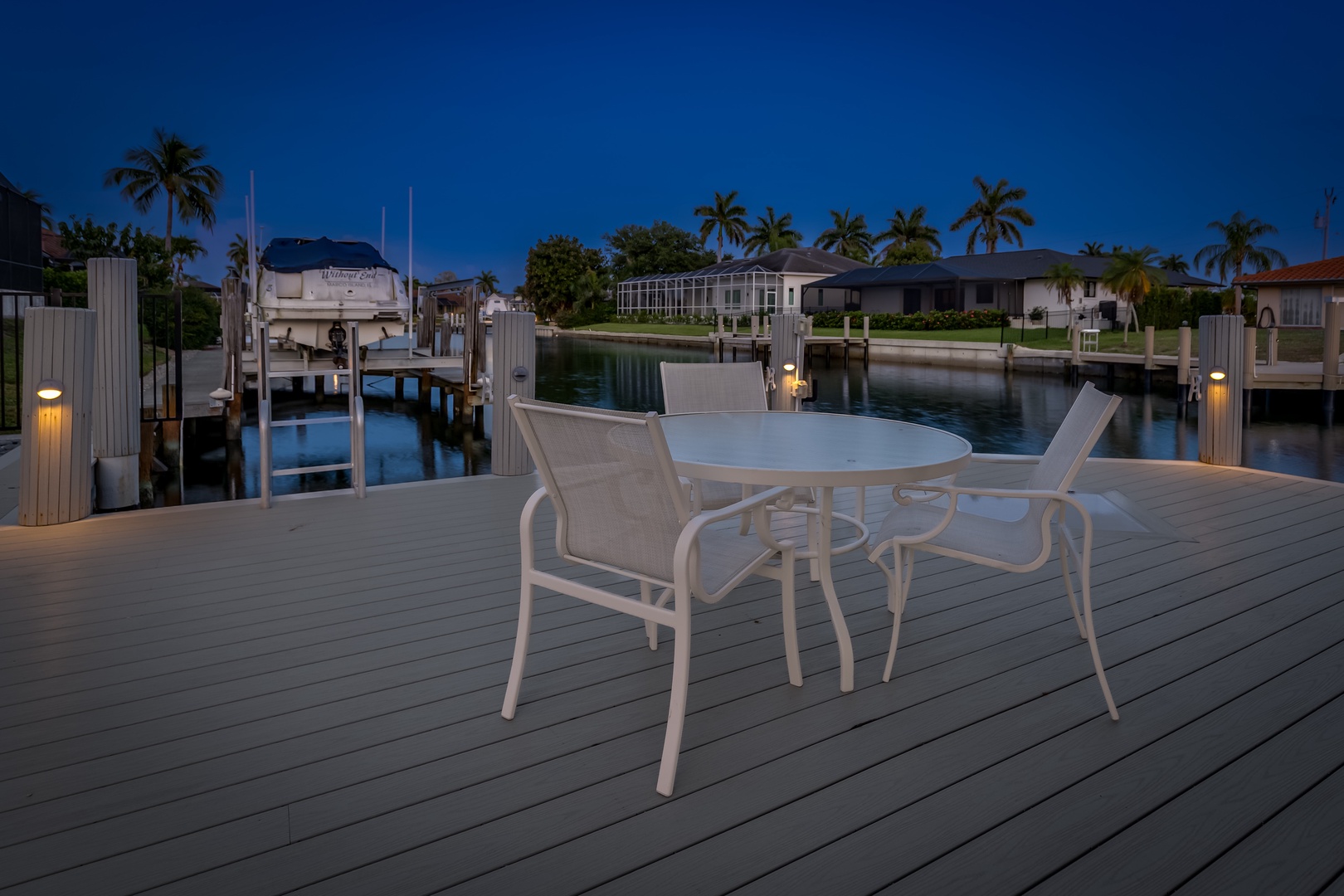 A private waterfront dock with direct boat access, outdoor seating, and soft ambient lighting overlooking a tranquil canal at twilight.