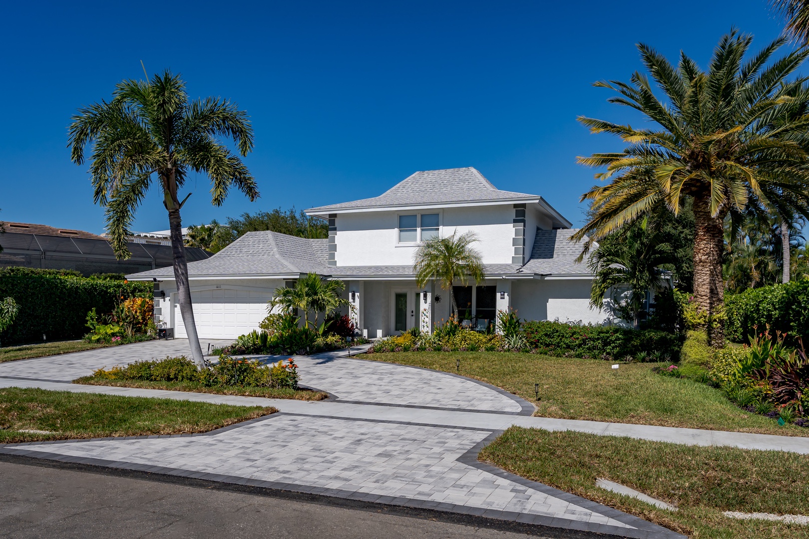 A modern tropical retreat featuring elegant white architecture surrounded by swaying palms and lush landscaping under brilliant blue skies.