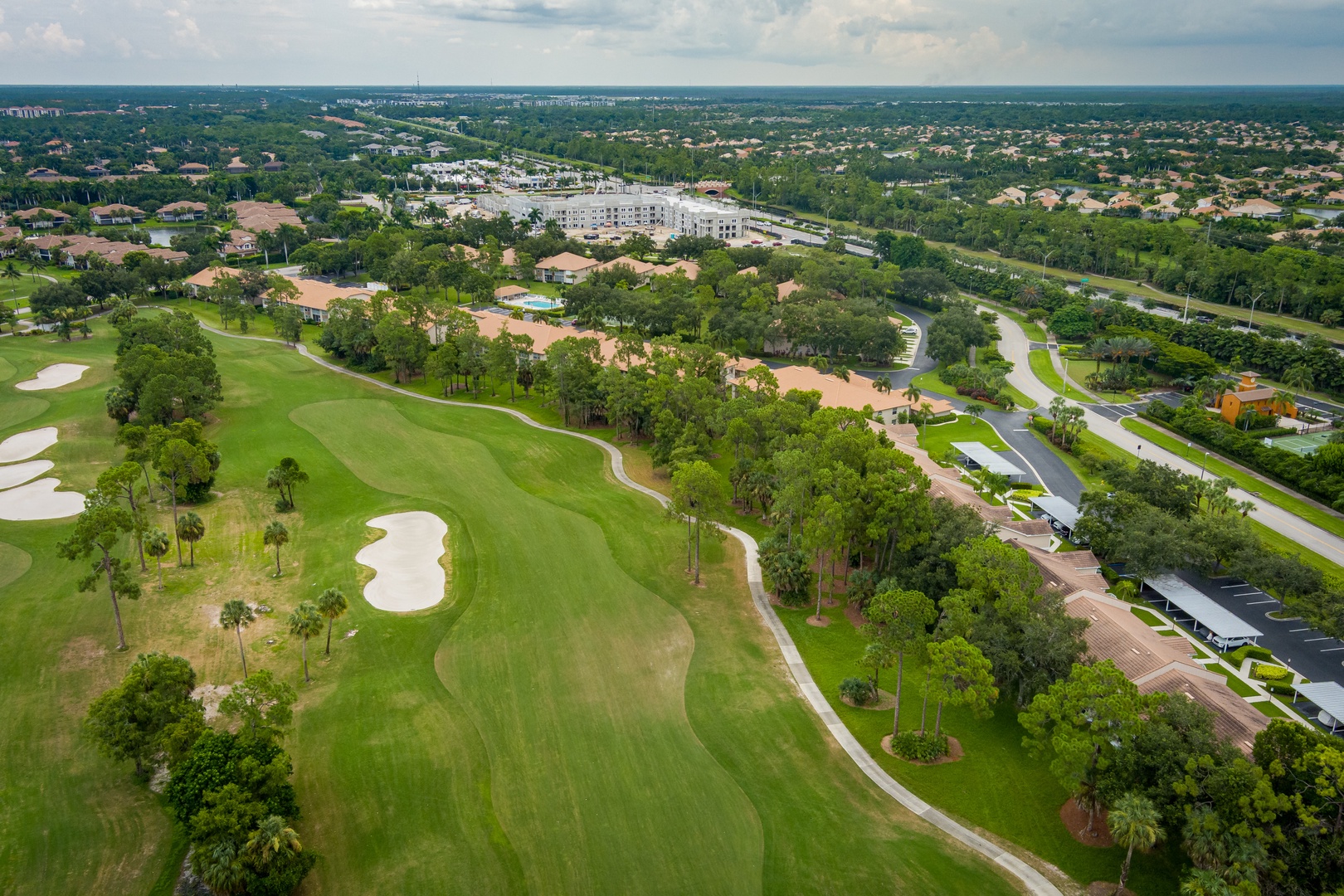 Aerial view showcasing the property's prime location adjacent to a championship golf course within a lush, tropical residential community, with easy access to local amenities and major roadways.