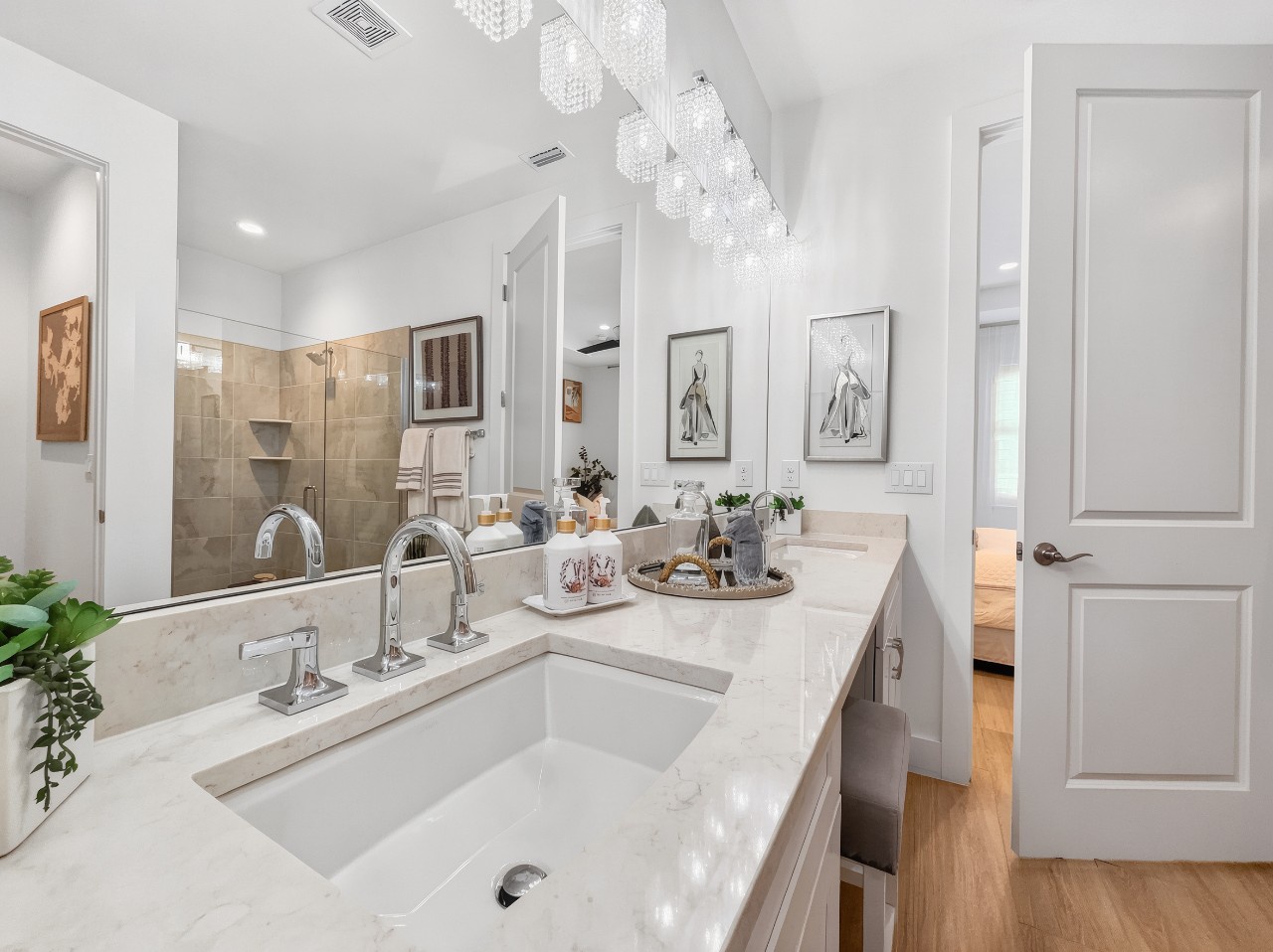 Bright spa-like bathroom featuring elegant dual vanities, gleaming marble countertops, and a sparkling chandelier. A serene retreat perfect after your adventures.