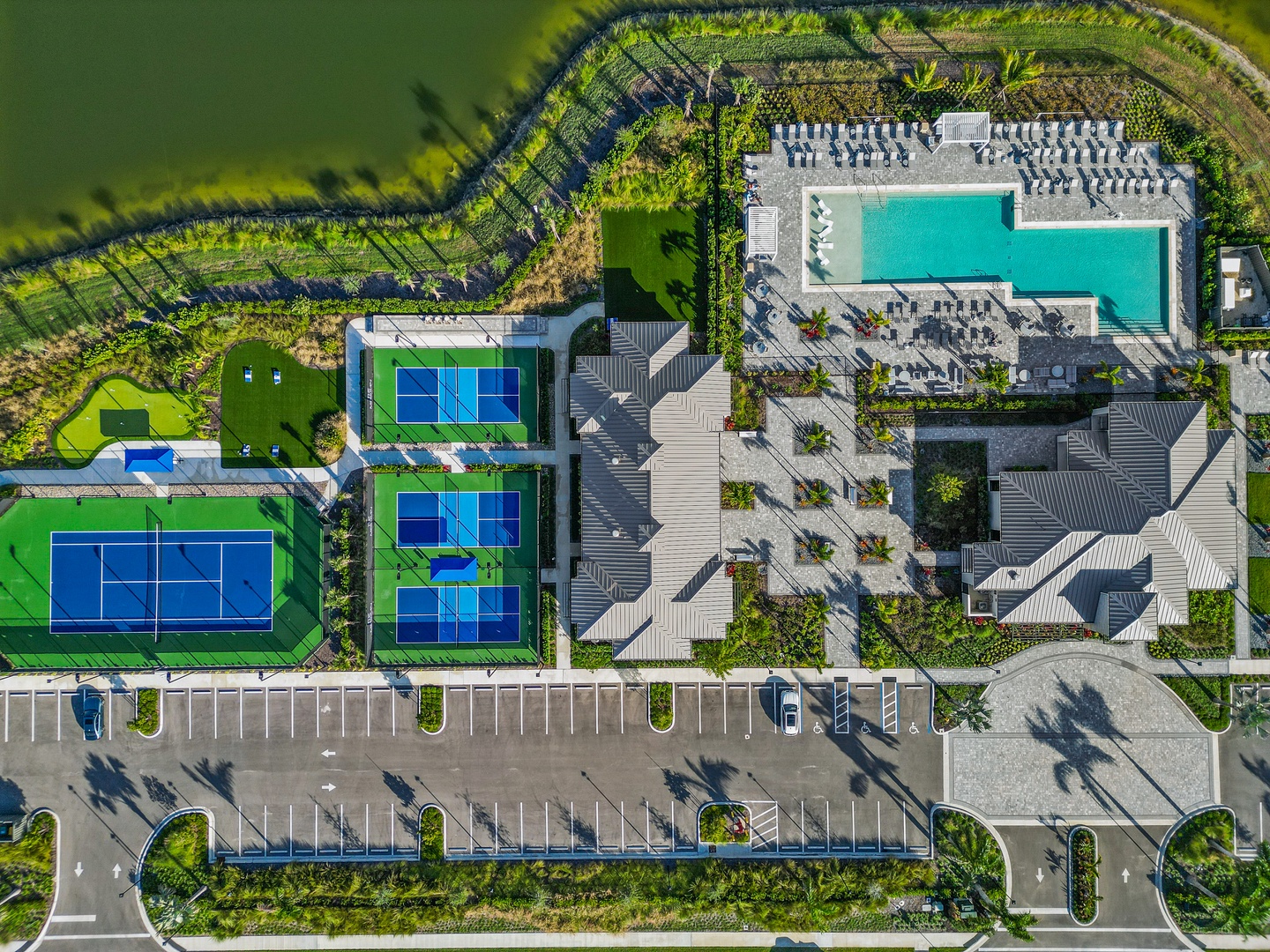 Aerial view of the property showcasing tennis courts, a sparkling swimming pool, landscaped grounds, and guest parking—a resort-style setting awaiting your arrival.