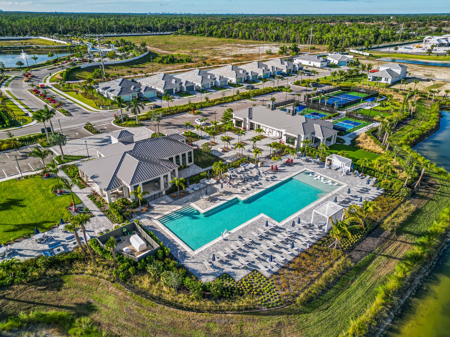 Aerial view of a modern vacation resort community featuring a sparkling pool, tennis courts, and tropical landscaping surrounded by natural wetlands and palm-filled greenery.