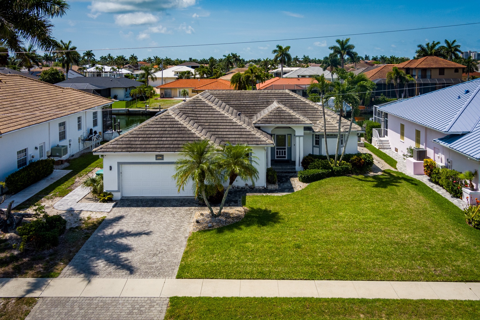 Aerial view of the vacation rental showcasing a charming single-story home with tropical landscaping, surrounded by palm trees and a peaceful residential neighborhood under sunny skies.