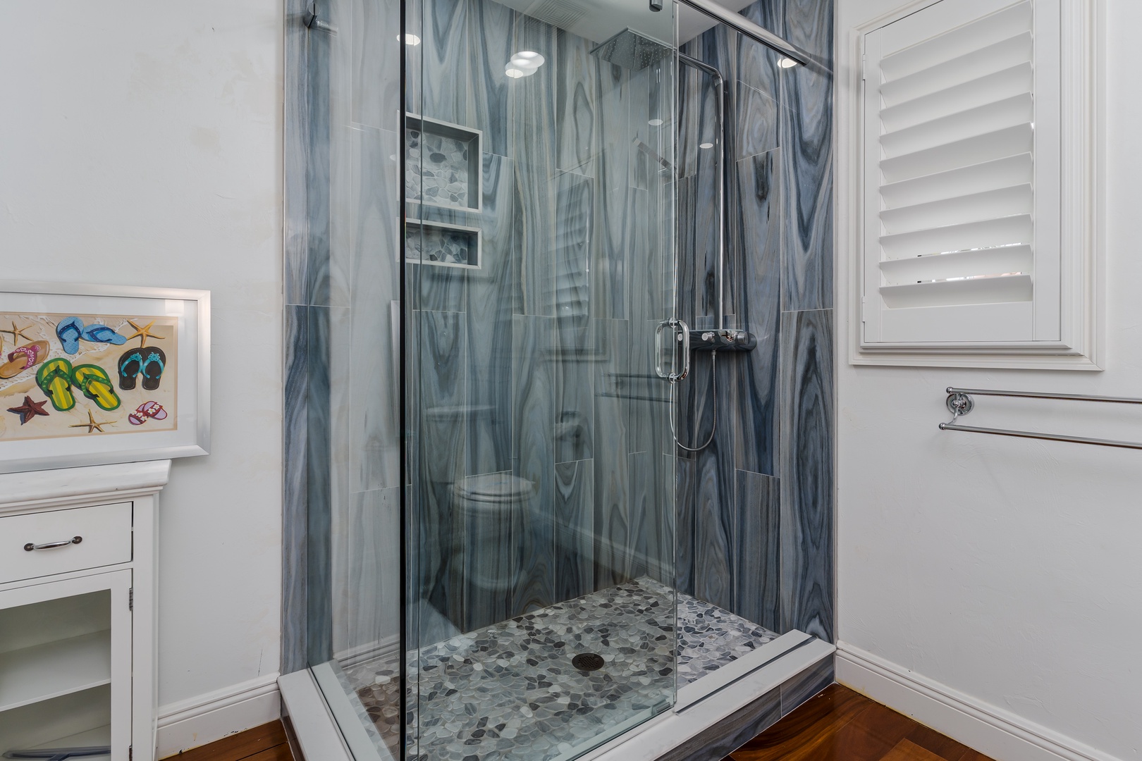 Step into your private glass-enclosed shower with beautiful blue swirl tile that evokes ocean waves. A mosaic floor and dual showerheads promise a refreshing, spa-like experience after a day at the beach.