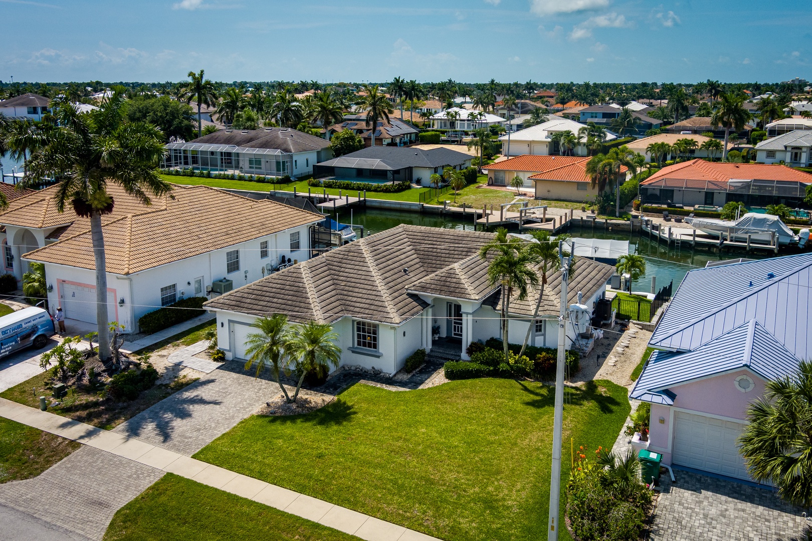 An elevated perspective showcasing the property nestled in a tranquil waterfront neighborhood with palm-lined streets, nearby canal access, and coastal Florida charm stretching to the horizon.