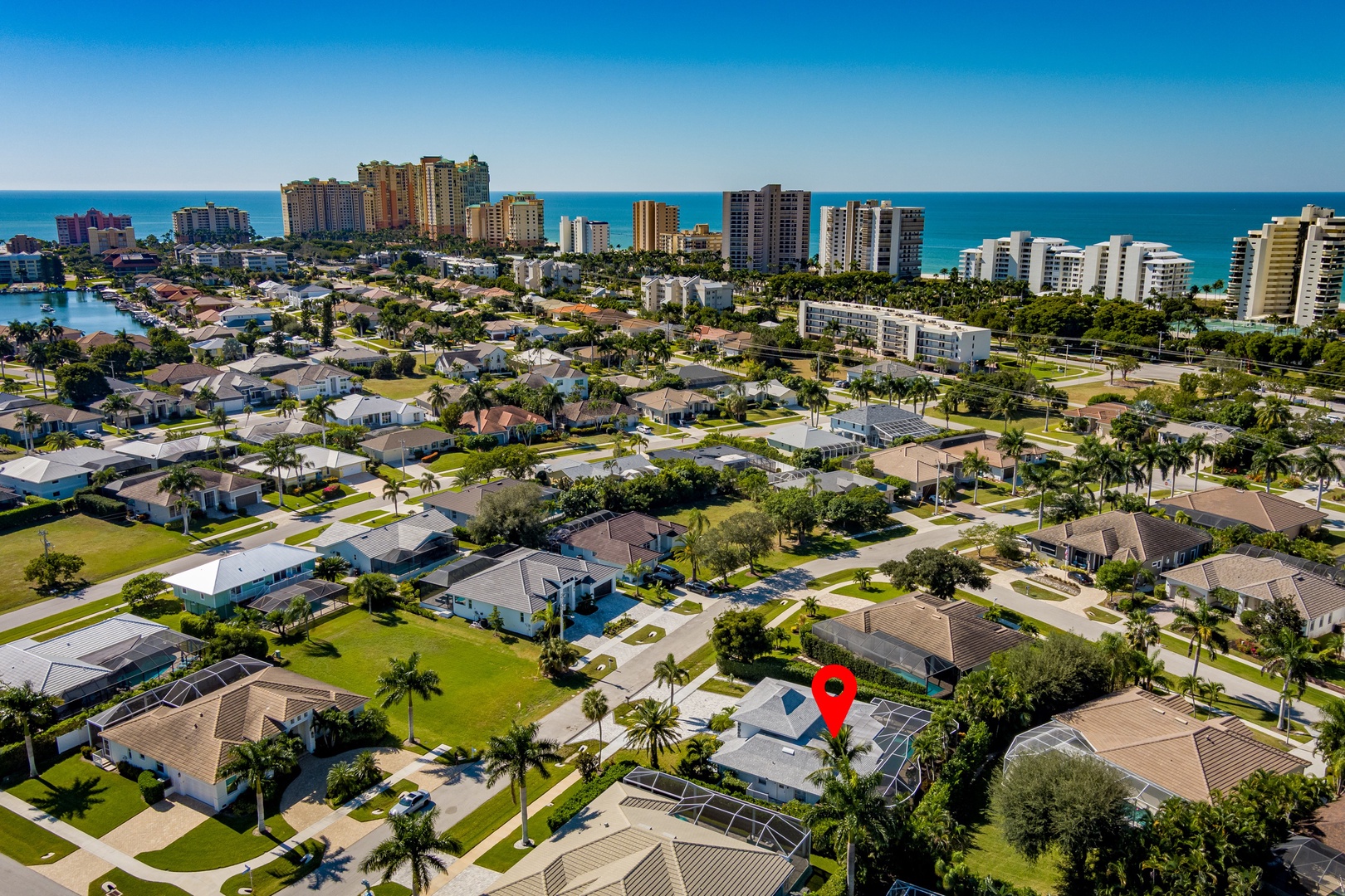 Aerial view of coastal neighborhood with residential homes, palm trees, and high-rise beachfront buildings near turquoise waters.