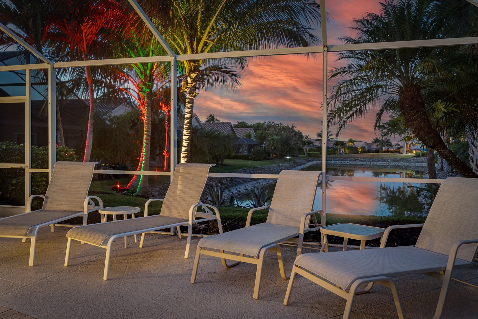 Sink into comfortable poolside loungers as vibrant sunset colors paint the sky through tropical palms, creating your perfect evening retreat.