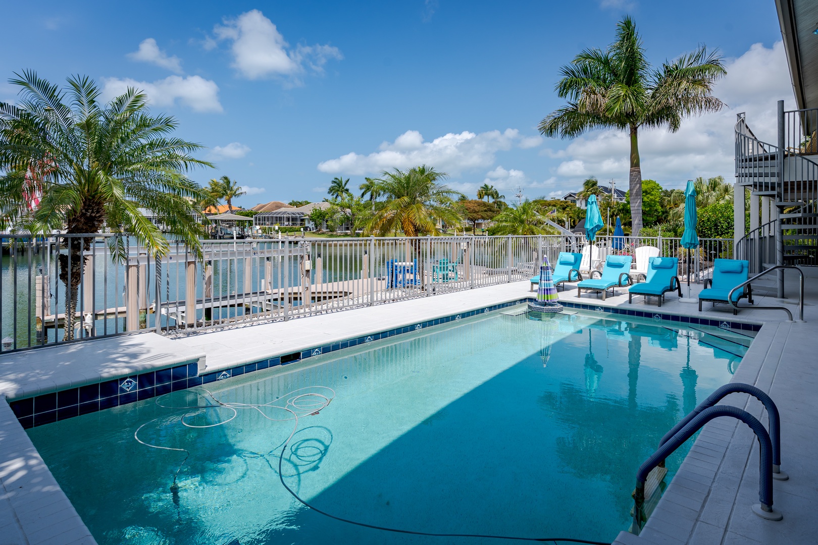 Waterfront pool deck with canal views and palm trees, offering a serene tropical escape near residential shores under bright blue skies.