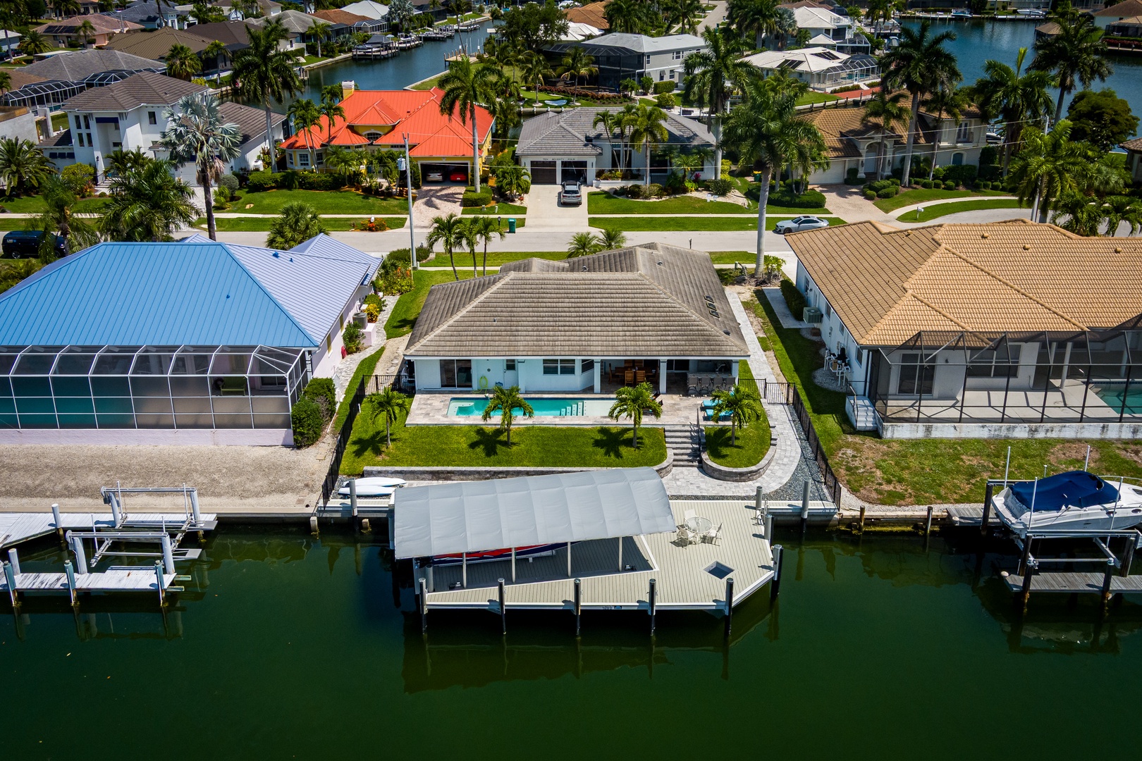 Aerial view of a waterfront vacation home with private boat dock and covered deck area, nestled in a palm-lined canal community offering direct water access and tropical Florida living.