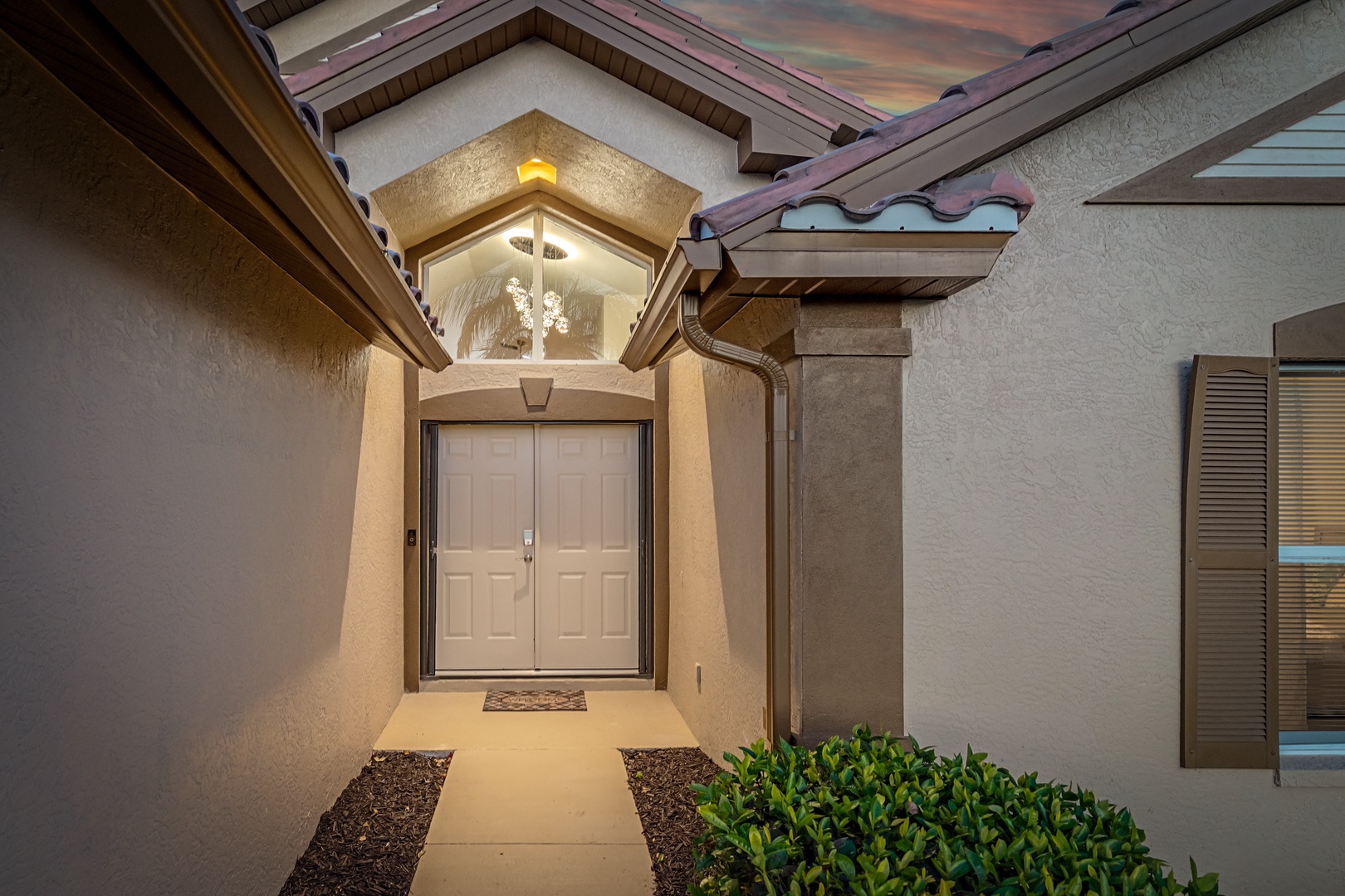 Elegant entrance showcases Spanish-style architecture with distinctive arched doorway, warm lighting, and professional landscaping welcoming arrivals.