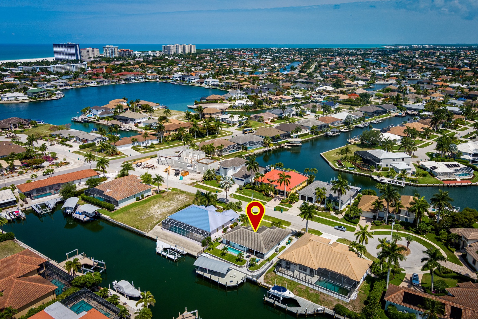 Aerial view showcasing the waterfront neighborhood with canal-front homes, palm-lined streets, and resort buildings along the coastline in the distance.