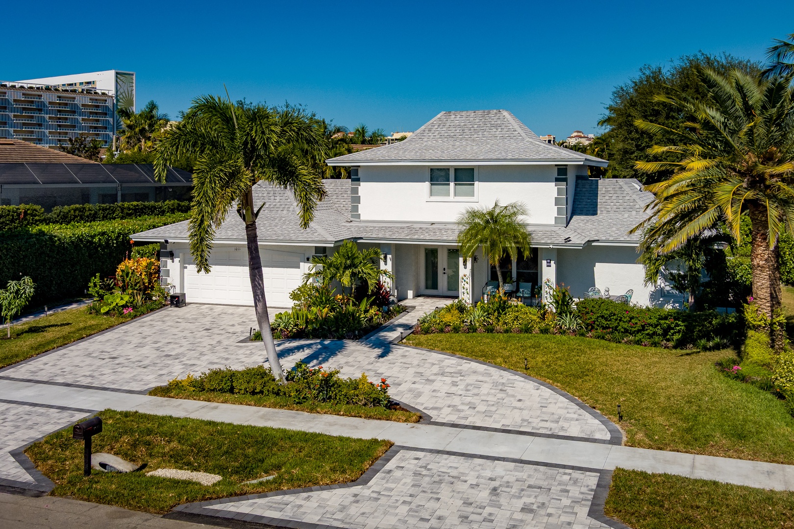 Modern white villa nestled among tropical palms with a curved paver driveway leading to the welcoming entrance.