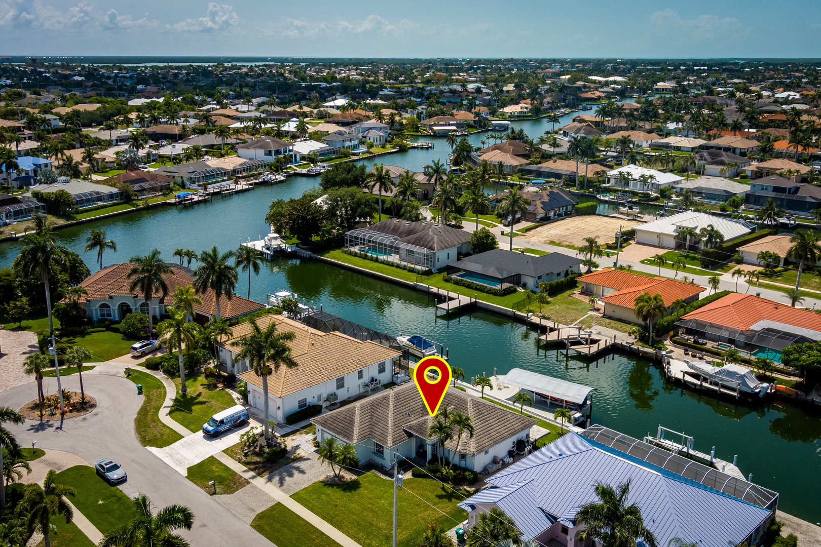 Aerial view of a waterfront neighborhood with canal-access homes, private boat docks, and palm-lined streets. The property is marked and situated among tropical coastal residences.