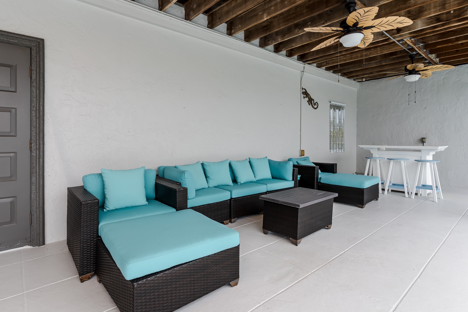 Unwind in your covered outdoor lounge, where vibrant turquoise cushions and tropical ceiling fans create a breezy oasis for relaxing afternoons and evening conversations.