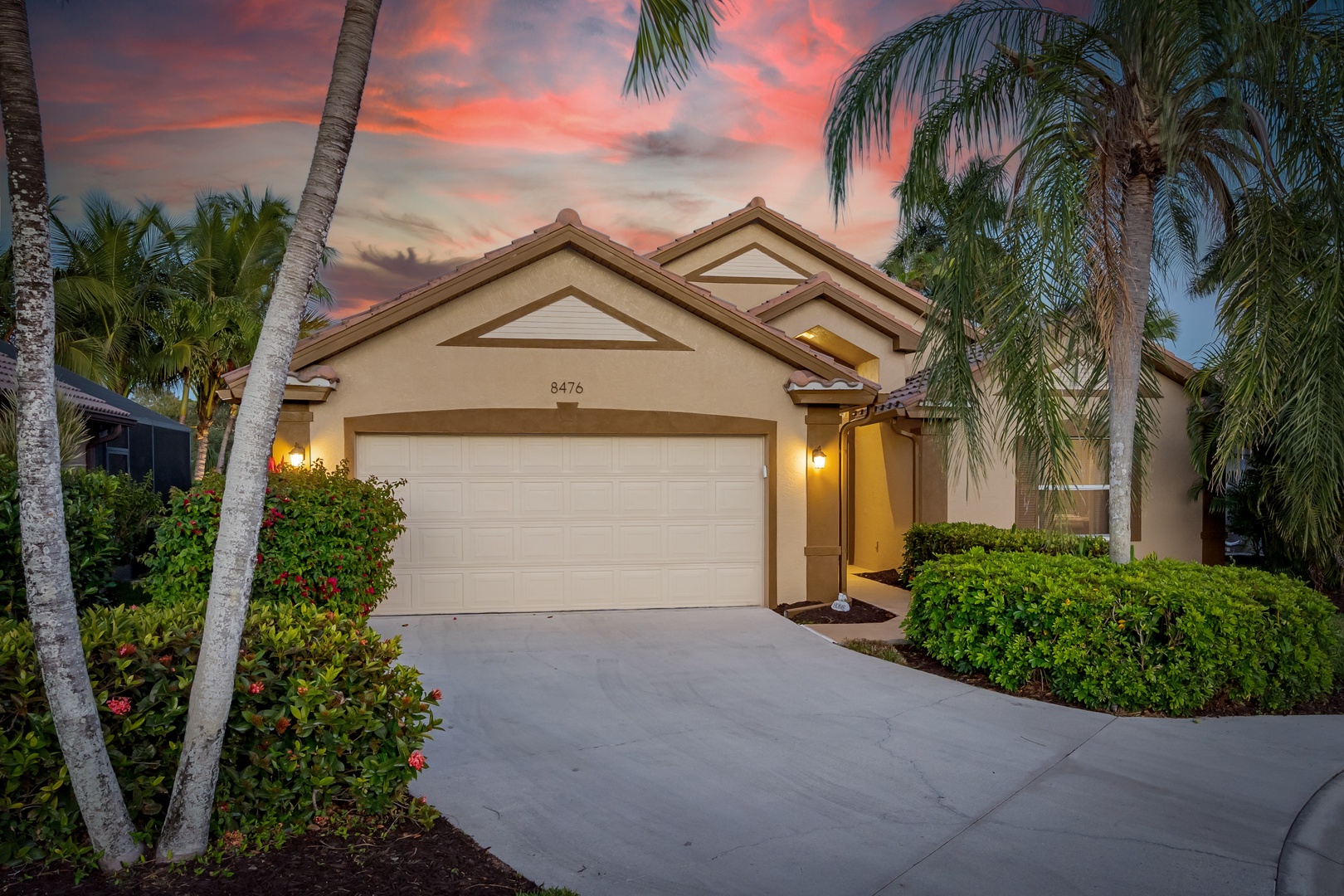 Elegant single-story vacation home nestled among swaying palms with a dramatic sunset painting the sky in vibrant coral and purple hues.