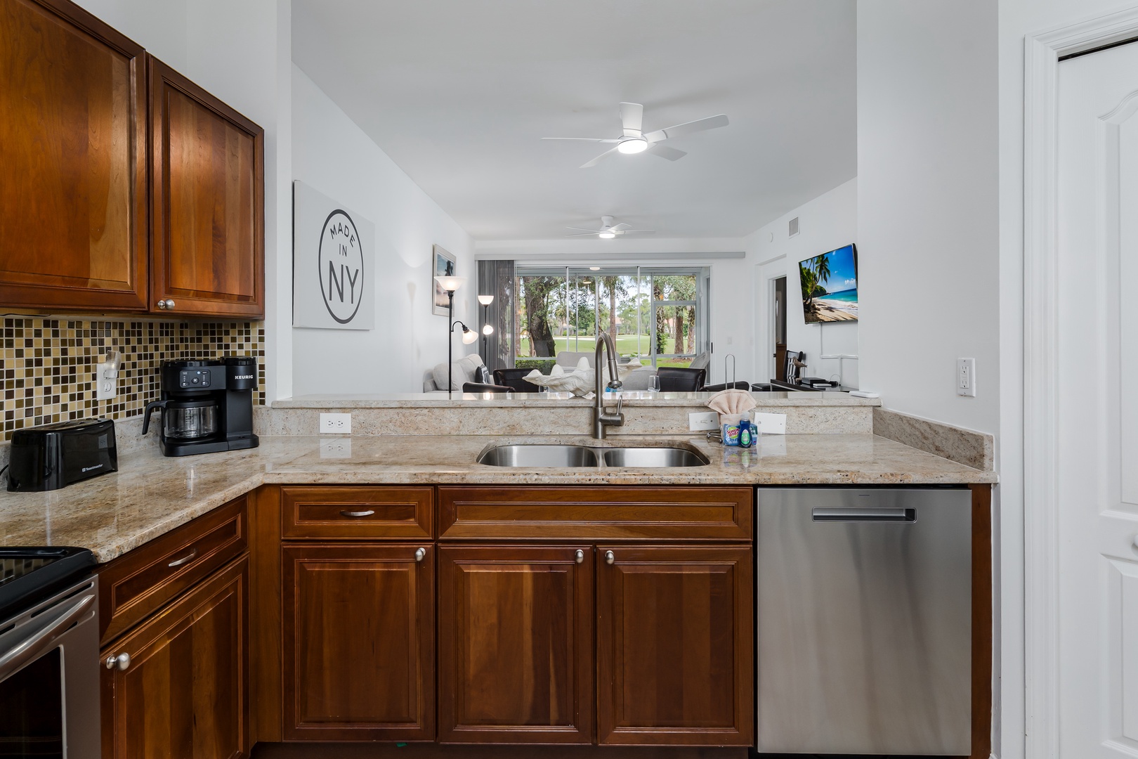 Fully equipped kitchen with granite countertops and modern appliances opens to the living area, flooded with natural light from windows overlooking peaceful grounds.