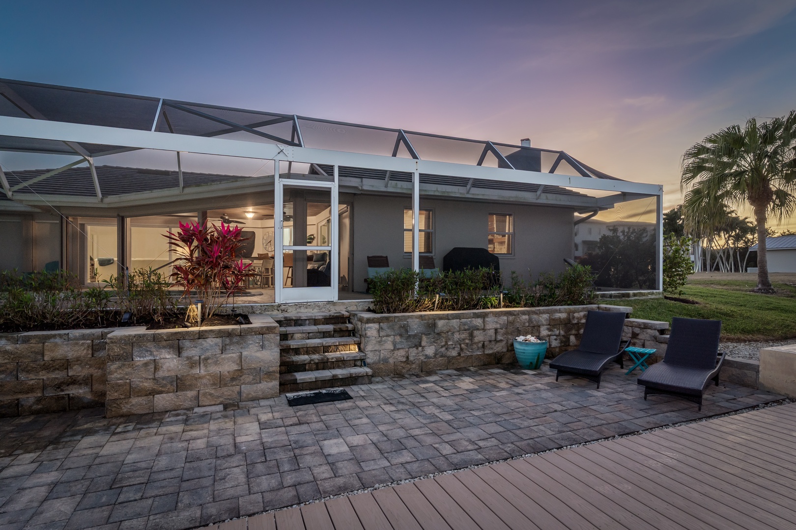 Modern waterfront home with screened patio and tropical landscaping captures stunning sunset colors.