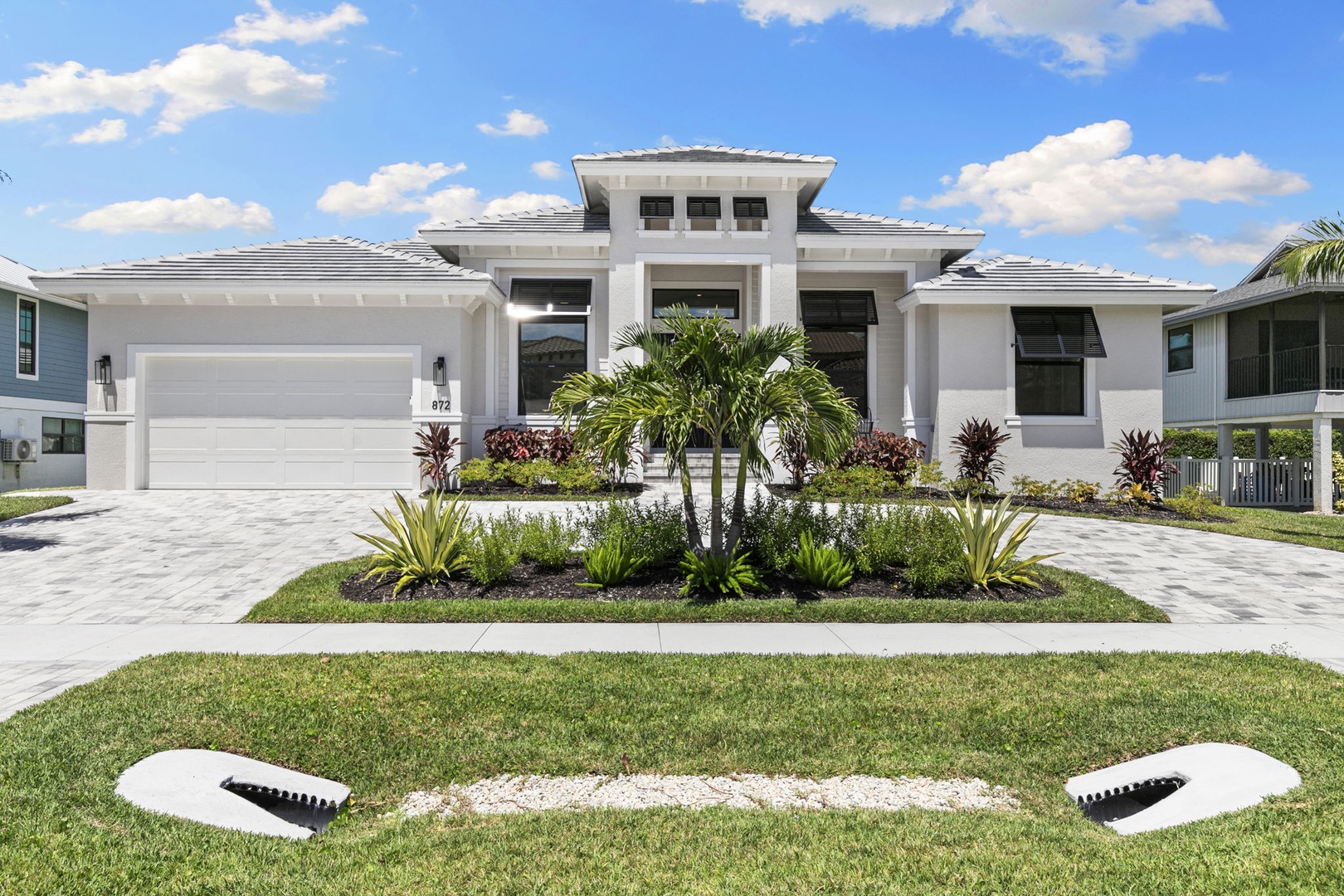 A modern coastal-style home with elegant white architecture, lush tropical landscaping, and a spacious driveway—the perfect Florida retreat for your getaway.