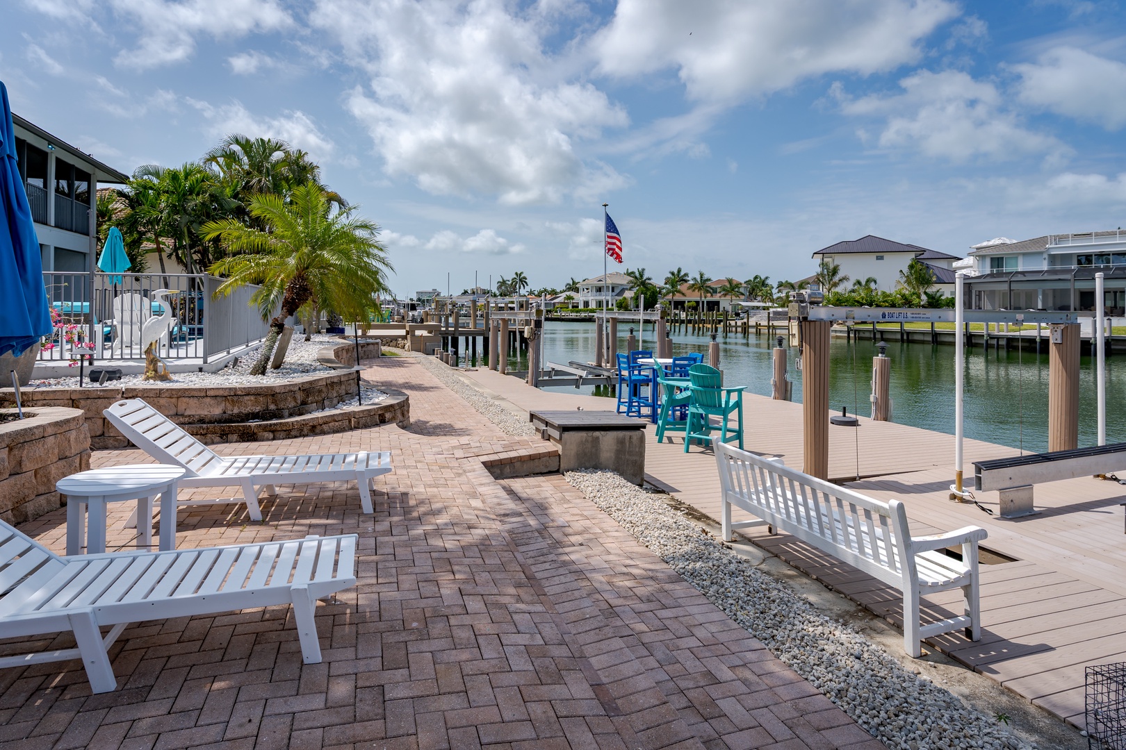 Waterfront property with private dock, canal access, and tropical landscaping. Multiple outdoor seating areas overlook the marina and neighboring homes under bright Florida skies.