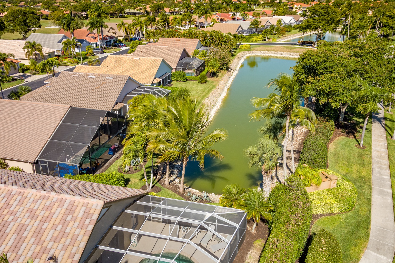 Aerial view of a waterfront vacation property featuring a private lake, screened pool area, and lush tropical landscaping in a quiet residential neighborhood.
