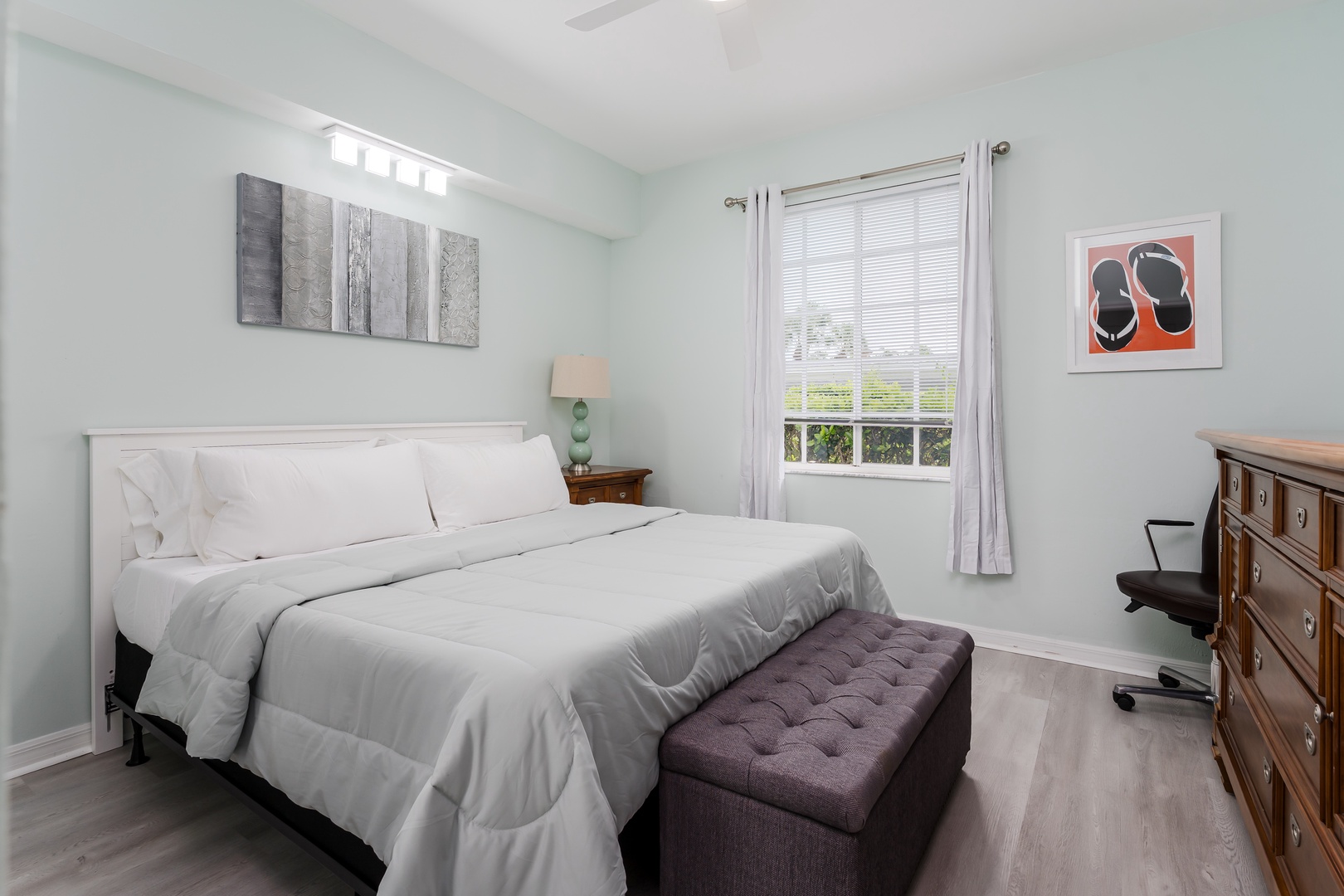 Wake up refreshed in this peaceful bedroom with crisp white linens, soft blue walls, and abundant natural light. A cozy tufted bench and workspace add comfort and convenience.