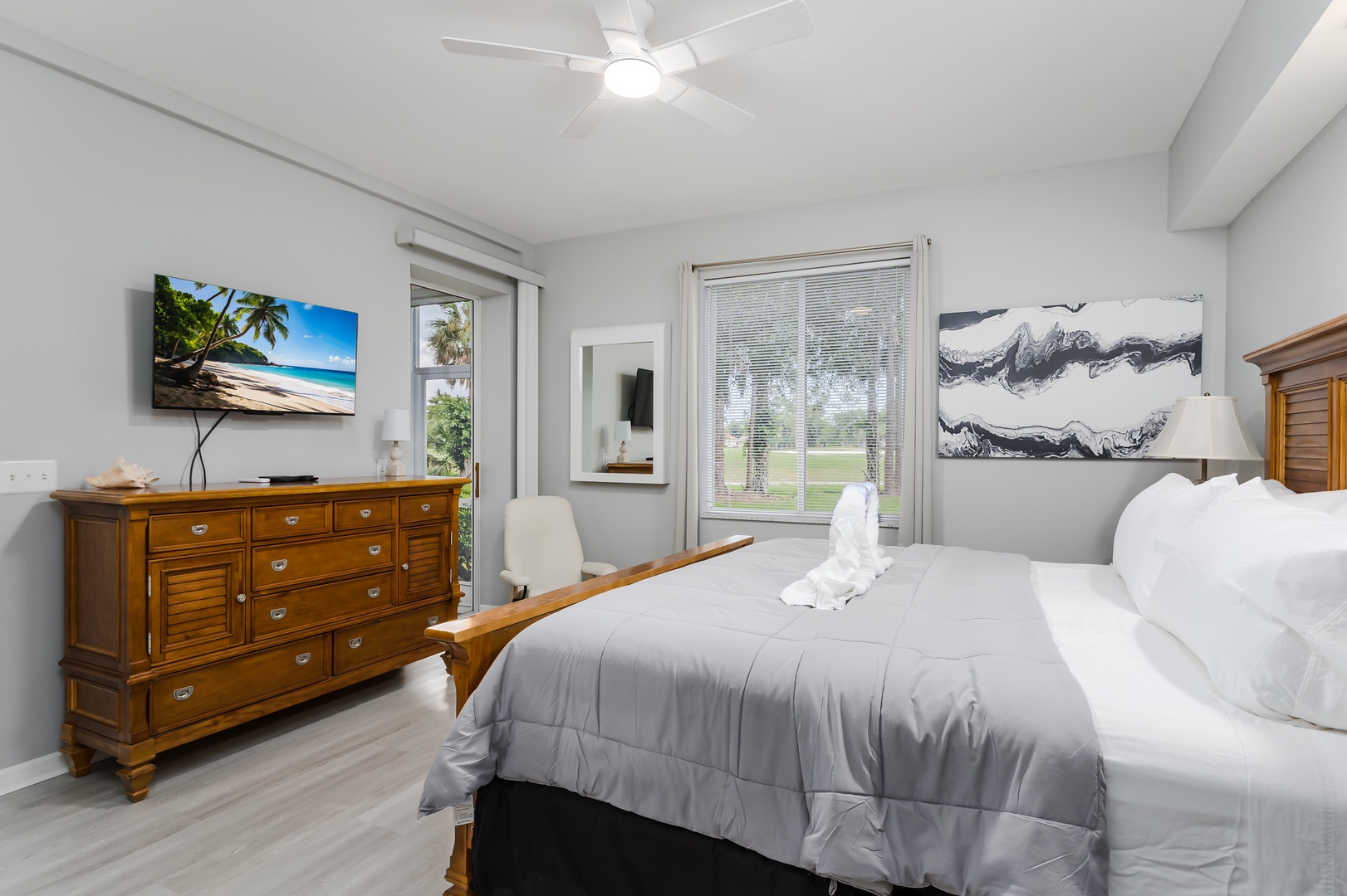 Your bright, serene bedroom features plush bedding, warm wood furnishings, and a ceiling fan to keep you cool. Natural light spills through the windows, offering peaceful views of the greenery outside.