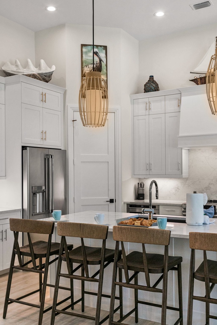 Step into a sun-filled kitchen where coastal charm meets modern convenience. Enjoy your morning coffee at the spacious island, surrounded by crisp white cabinetry and warm natural textures that make cooking feel like a breeze.