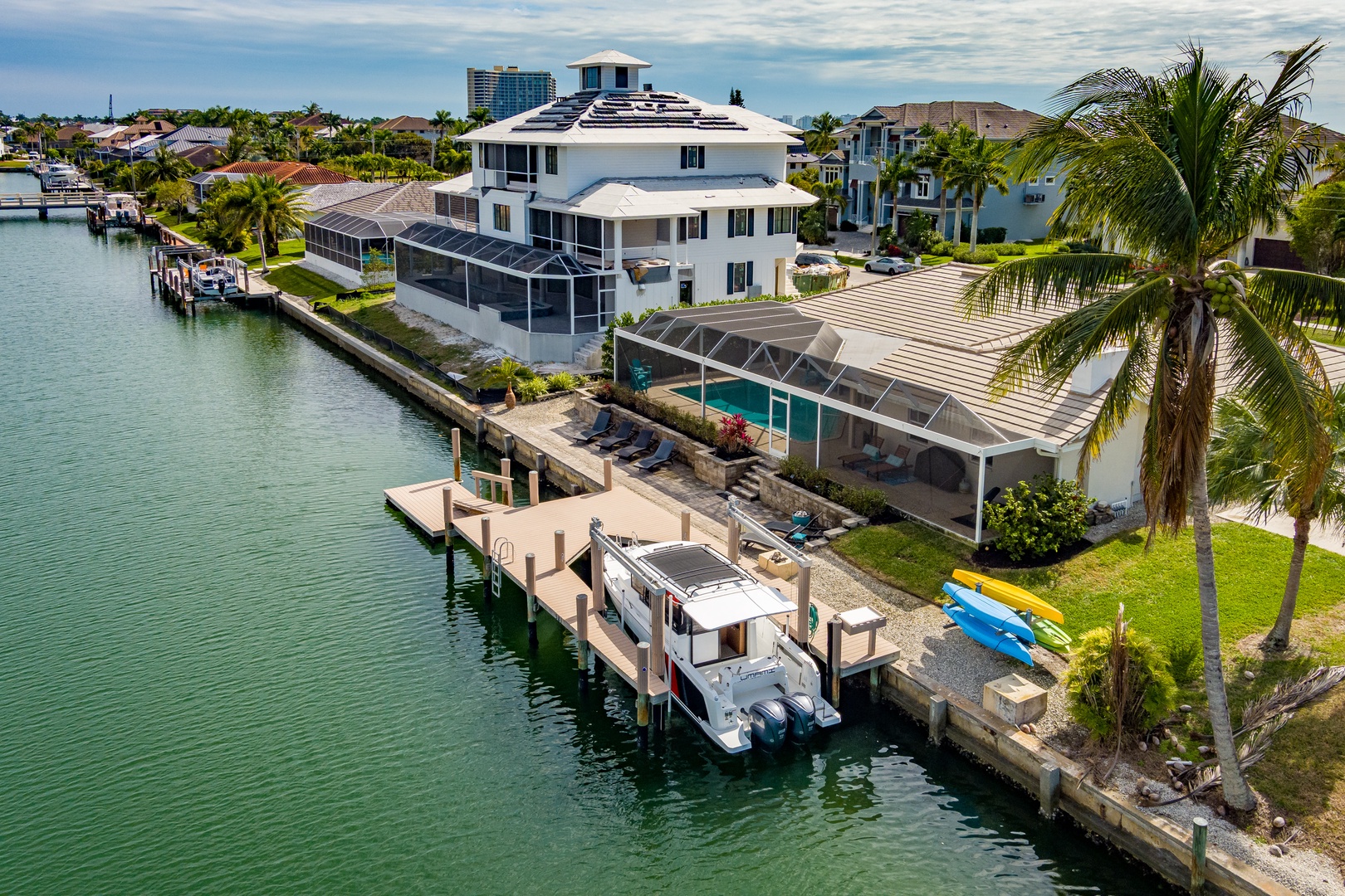 Stunning waterfront luxury home with private dock, boat, and kayaks on tranquil canal waters surrounded by tropical palms.