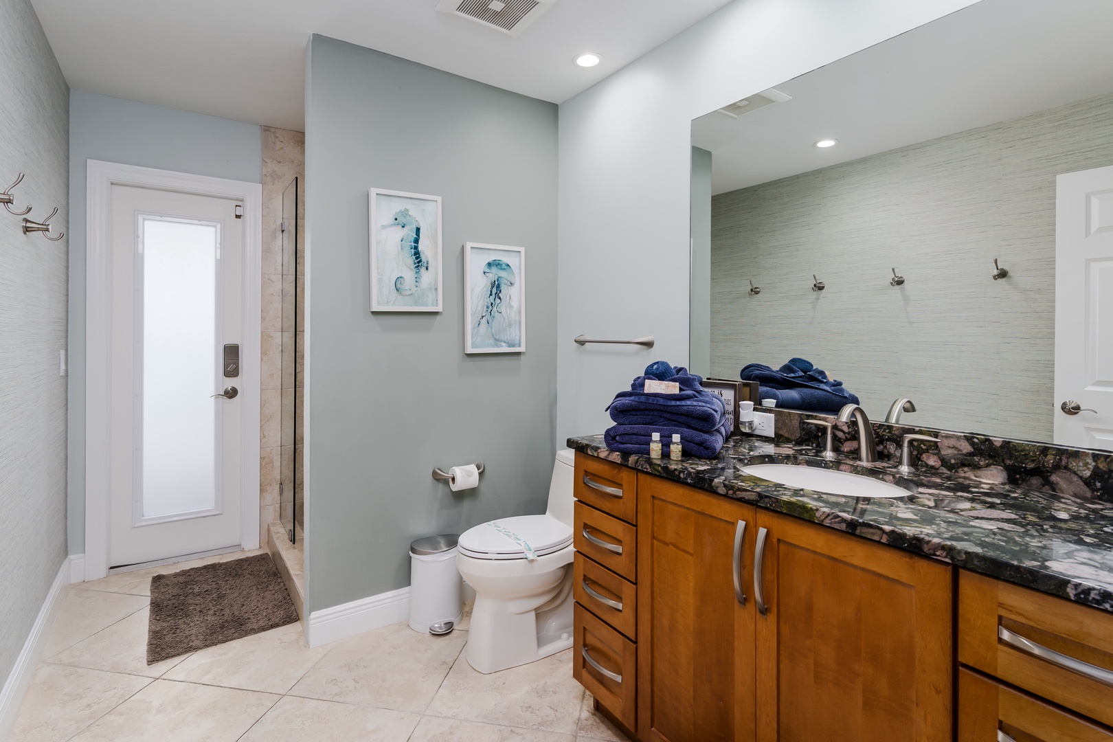 Step into your spa-like bathroom with granite counters, plush navy towels, and elegant coastal artwork creating a serene retreat.