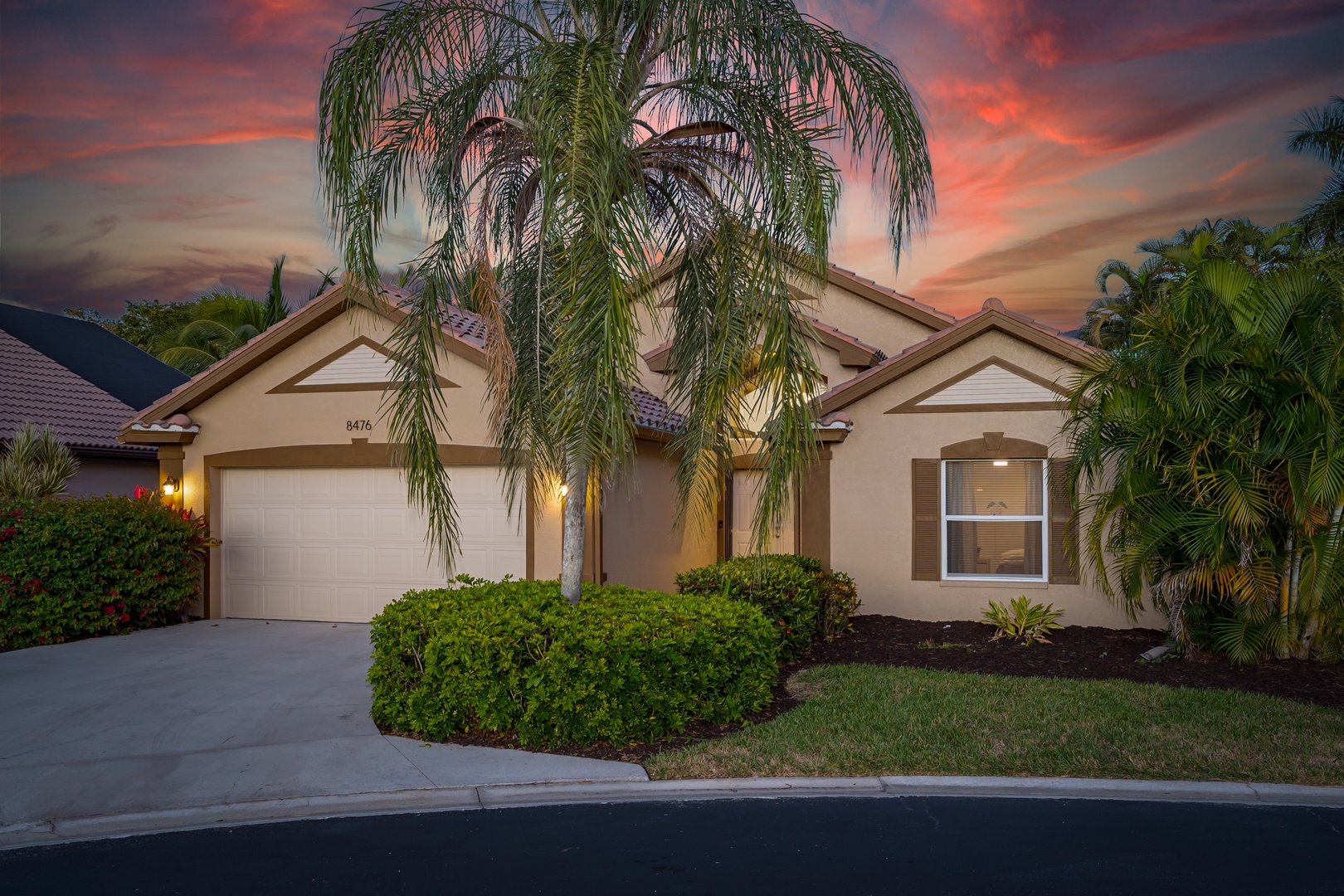 Elegant single-story home with tropical landscaping and dramatic sunset backdrop creating a stunning arrival experience.