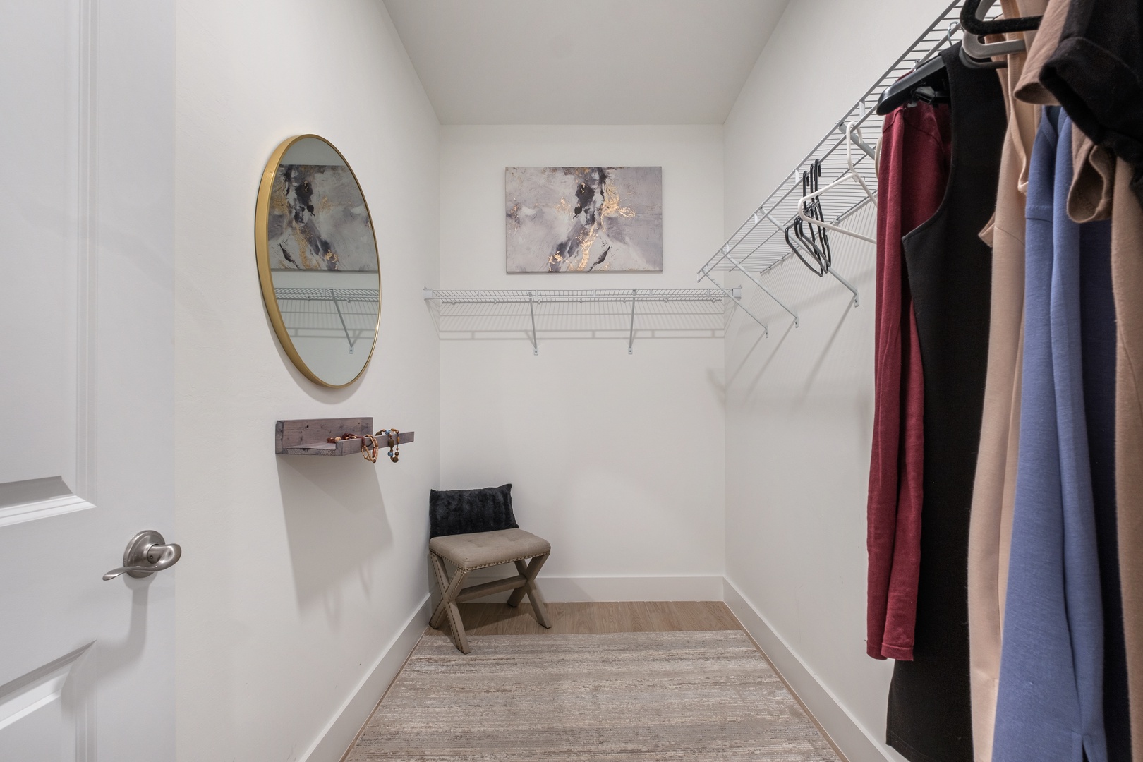 Your spacious walk-in closet offers organized storage with wire shelving, a cozy bench for getting ready, and thoughtful touches like artwork.