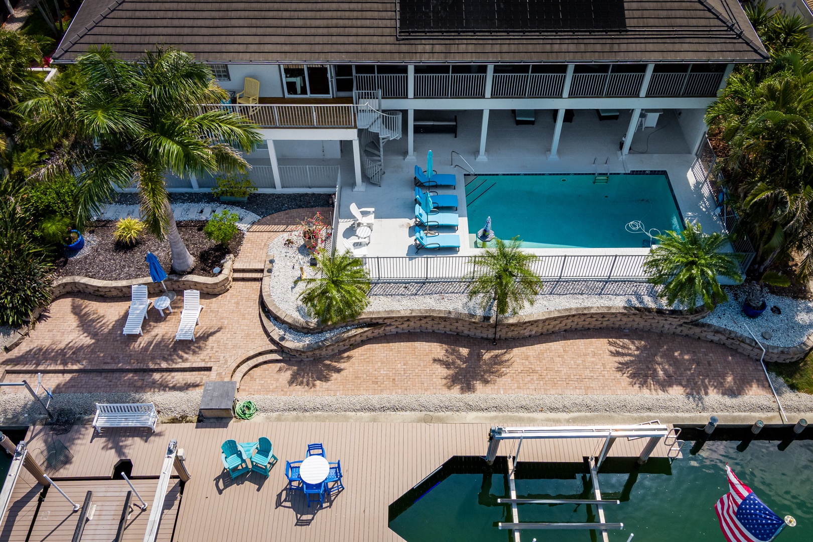 Aerial view of a waterfront vacation home featuring a private pool, spacious patio areas, tropical landscaping with palm trees, and direct dock access to the canal.