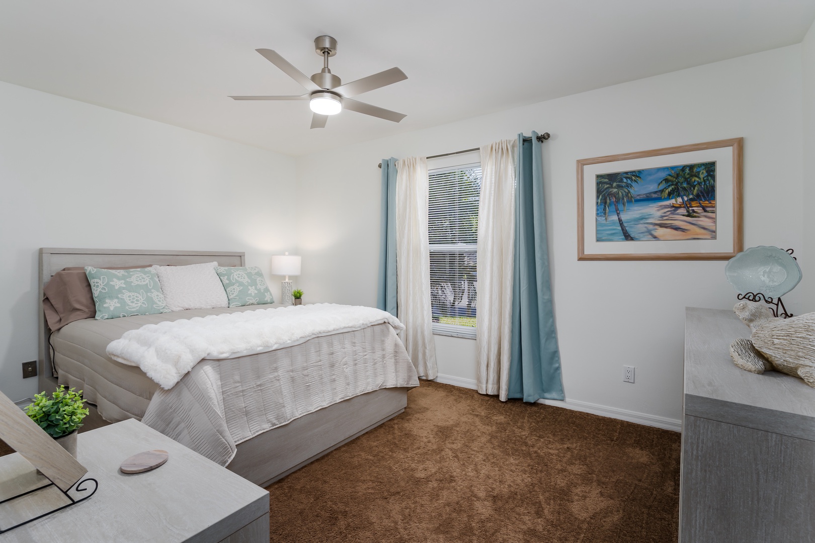 Drift off peacefully in your comfortable bedroom featuring soft linens, tropical artwork, and a gentle ceiling fan for perfect climate control.