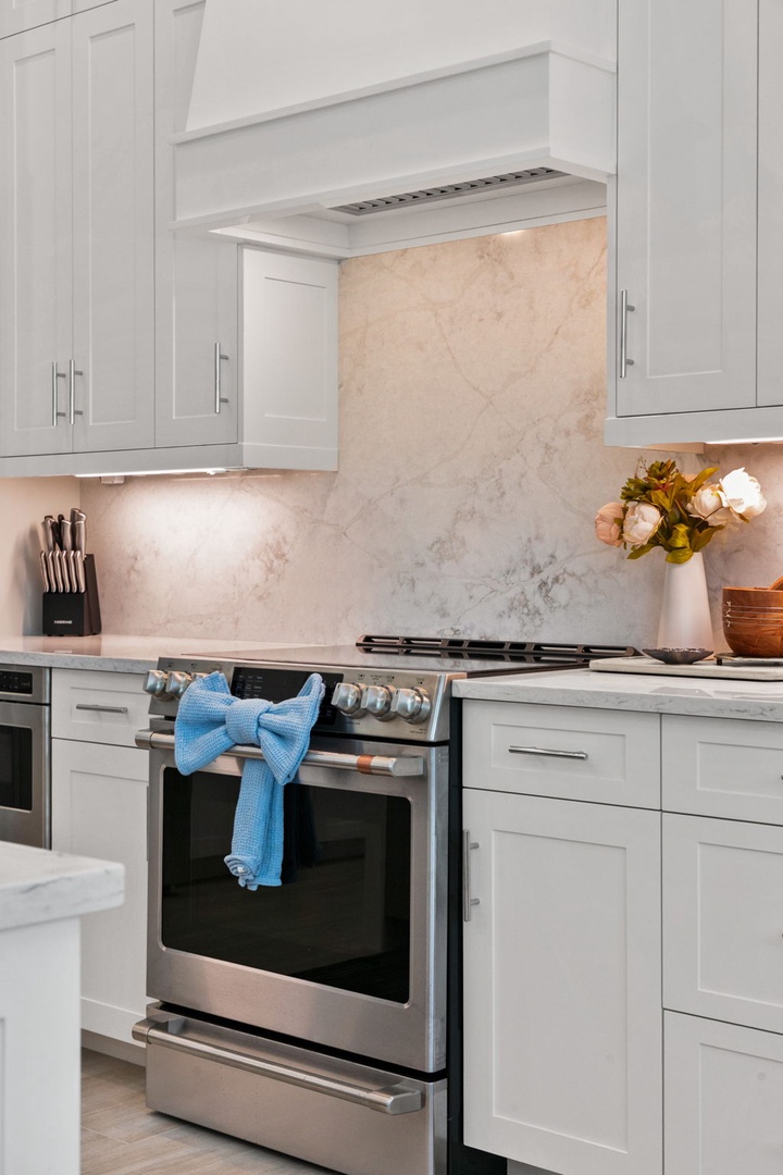 Picture yourself preparing a gourmet meal in this bright, fully-equipped kitchen with beautiful marble backsplash and modern stainless steel appliances. Fresh flowers and thoughtful design touches make your cooking experience feel special.
