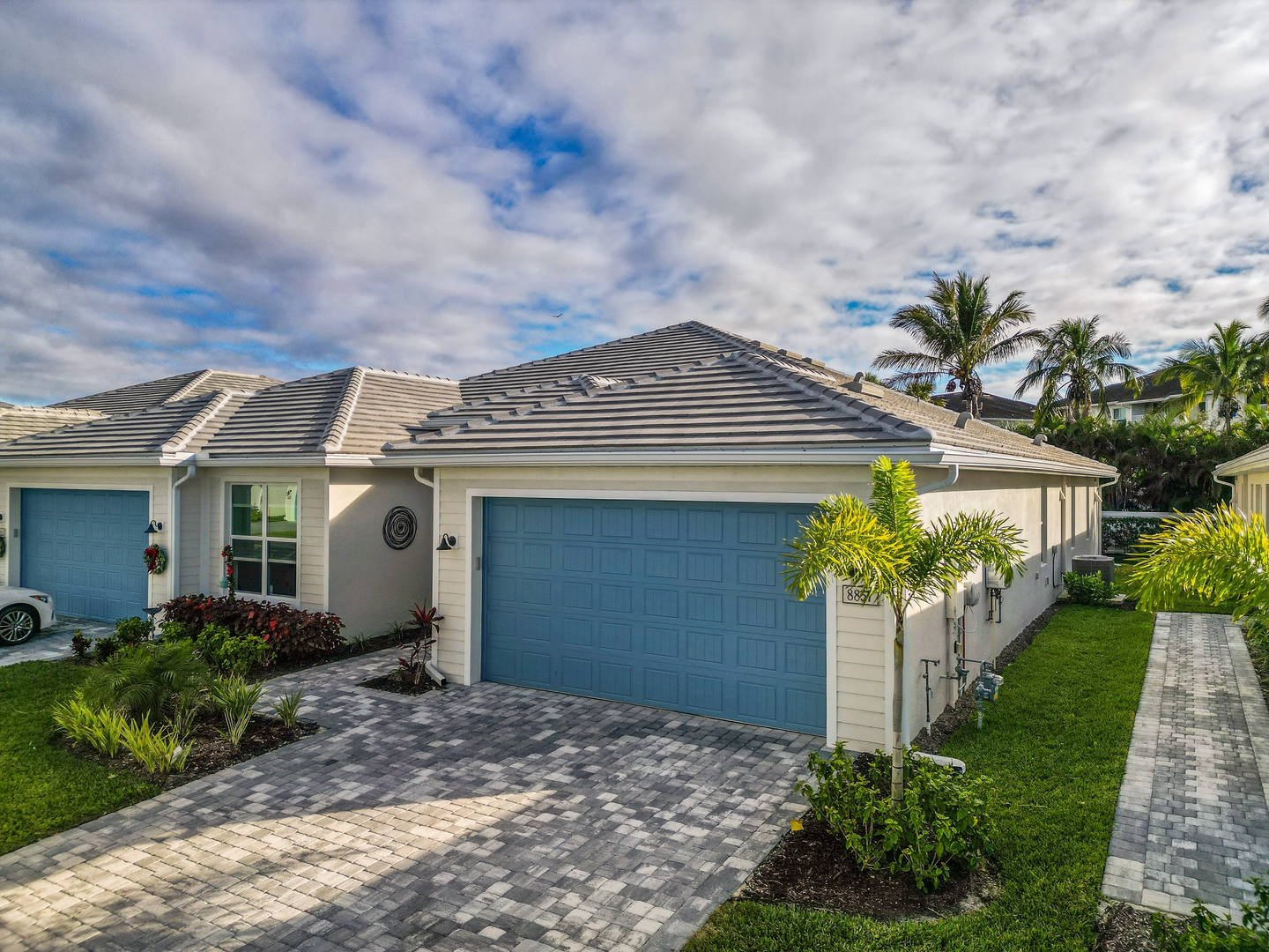 Modern single-story home with tropical landscaping and paved driveway in a residential neighborhood setting.