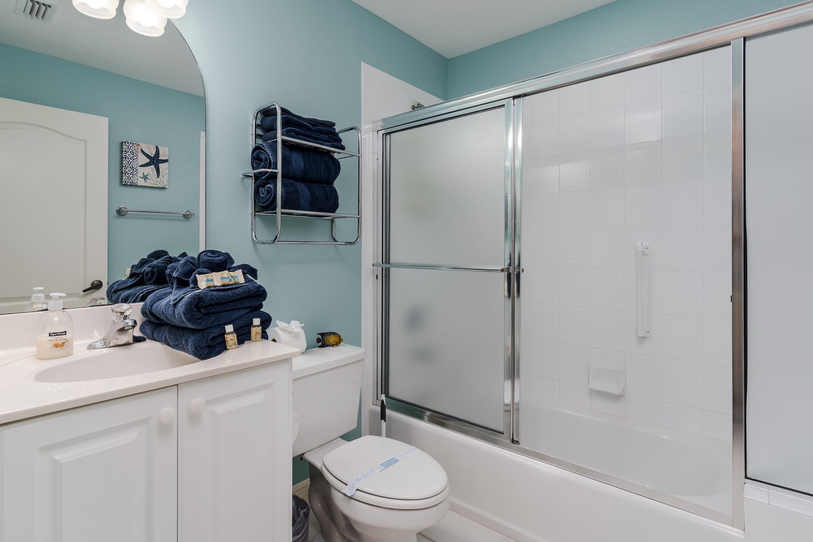 Relax after a long day in your pristine bathroom, featuring a spacious tub-shower combo with glass doors and plush navy towels waiting for you.