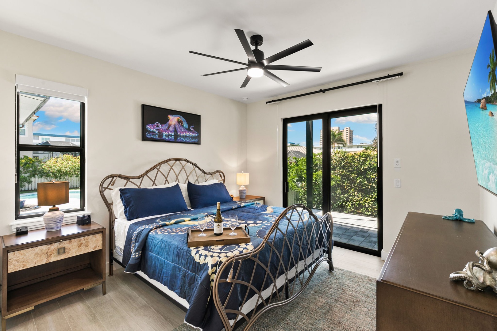Unwind in your bright bedroom with a plush bed, modern ceiling fan, and calming ocean-inspired decor. Windows overlook lush greenery for a peaceful retreat after each day's adventures.