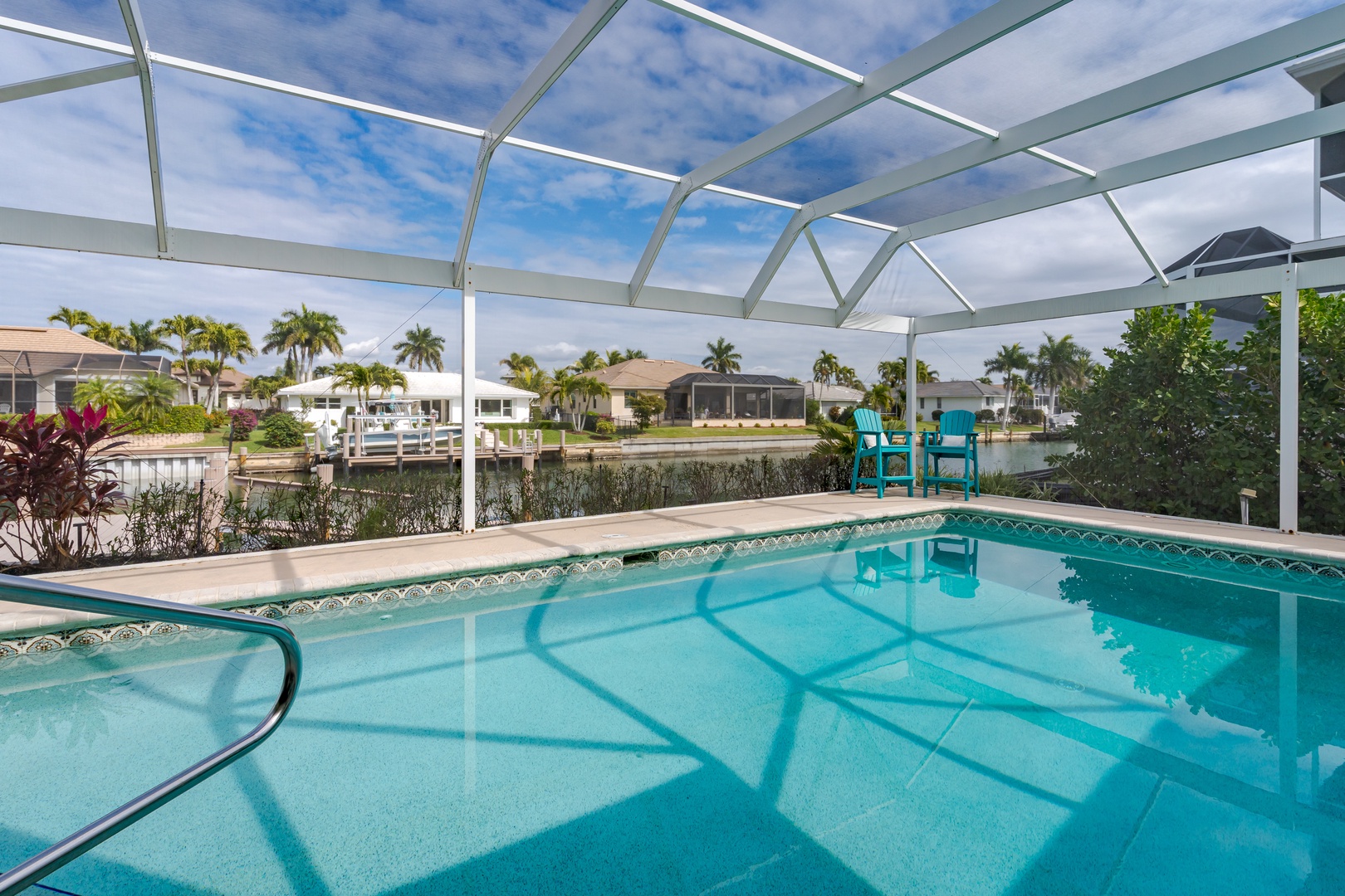 Dive into your private screened pool while enjoying panoramic canal views with neighboring homes and palm trees creating a tropical backdrop.