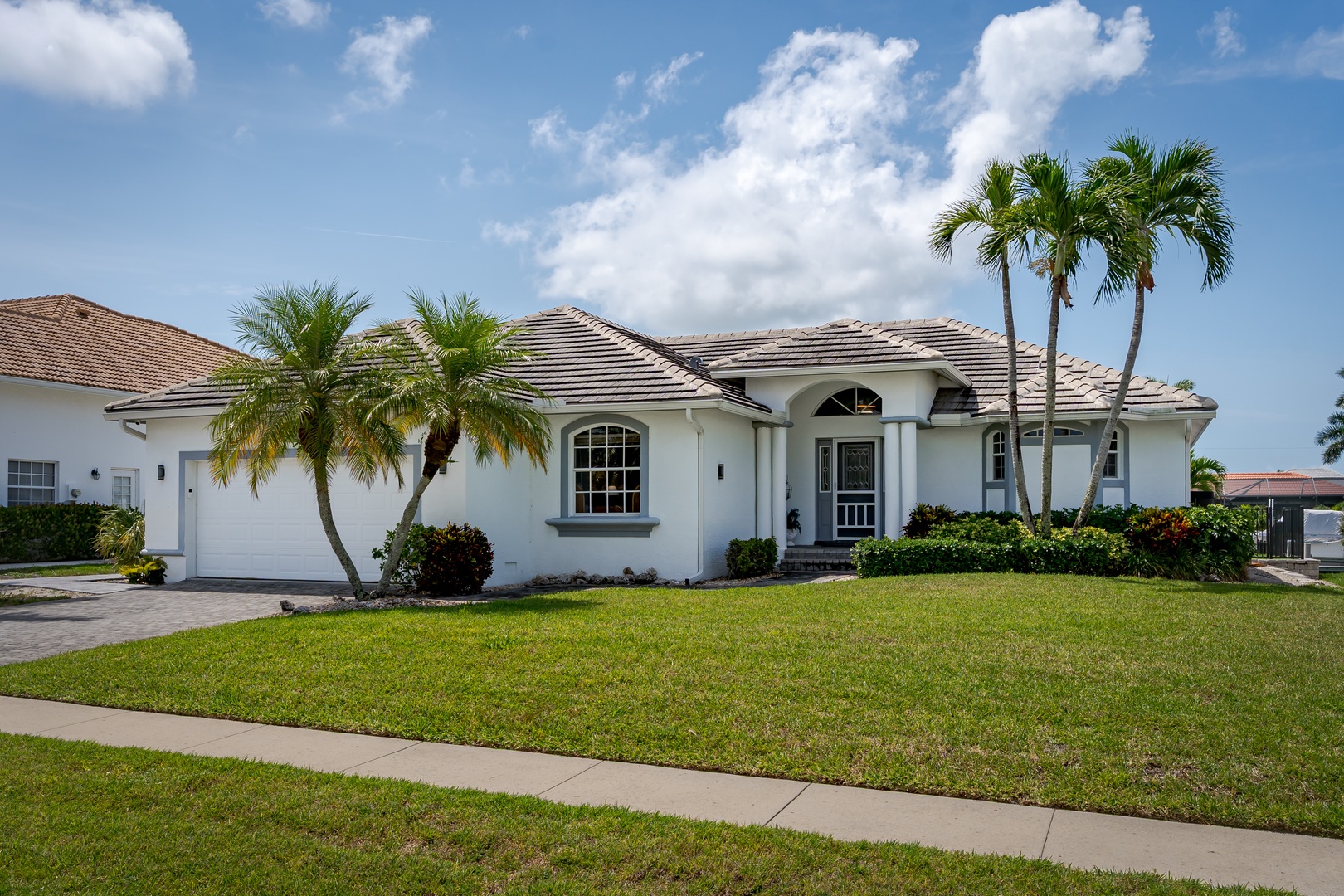 A beautiful single-story home with elegant white stucco, arched windows, and mature palms set in a quiet residential neighborhood beneath brilliant Florida skies.