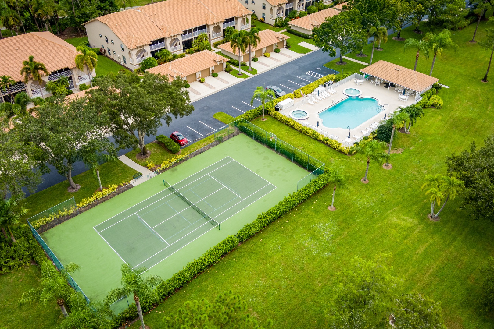 This aerial view showcases the property's resort-style amenities, including a refreshing pool, tennis court, and lush tropical grounds, all surrounded by verdant landscaping and convenient parking.