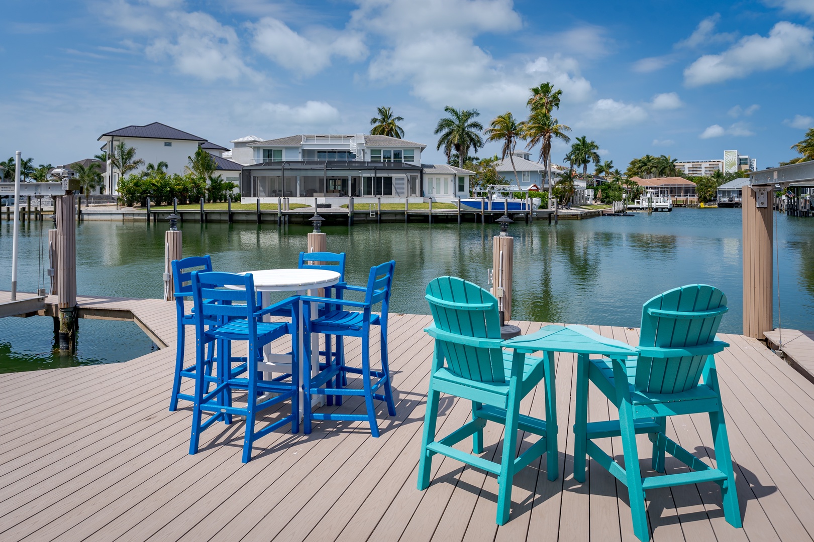 Private waterfront dock with vibrant seating overlooking serene canal, modern homes, and swaying palms—the perfect spot for morning coffee or sunset cocktails with your favorite people.
