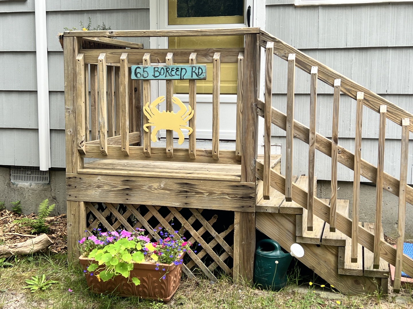 Charming beach cottage entrance with crab-adorned deck and blooming garden welcomes you to coastal comfort.