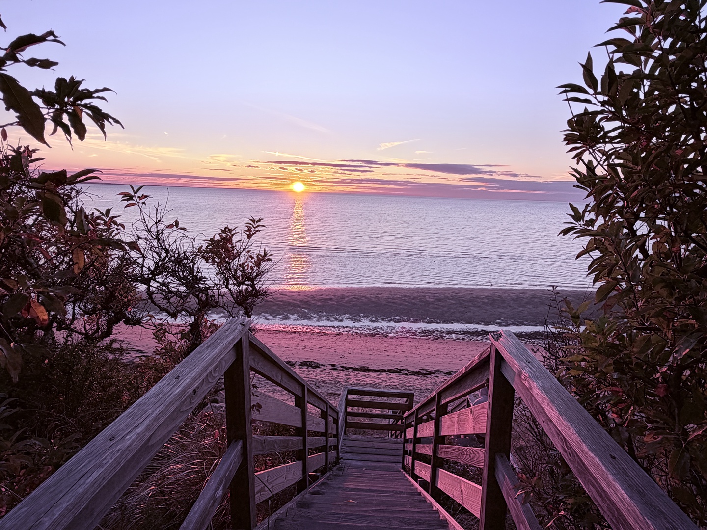 Stunning sunset paints the sky in vibrant hues over pristine beach access via wooden boardwalk through coastal vegetation.