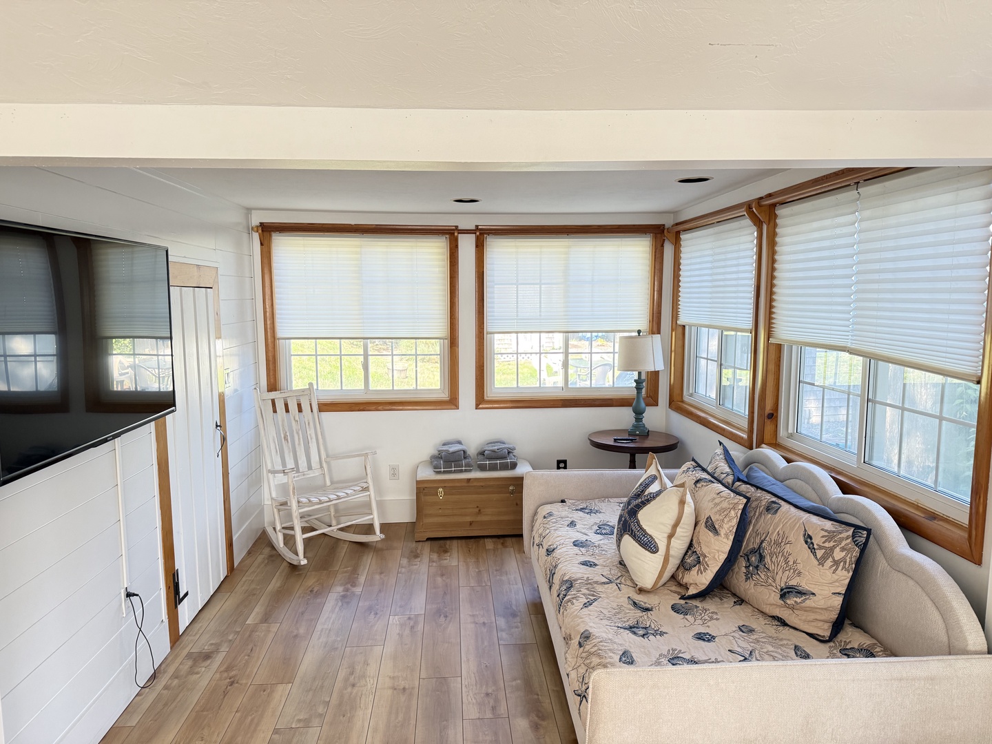 Settle into your sunny living room, where a soft couch invites you to relax beneath walls of windows. Feel the coastal breeze, rock gently in your chair, and let the bright natural light fill your space with warmth.
