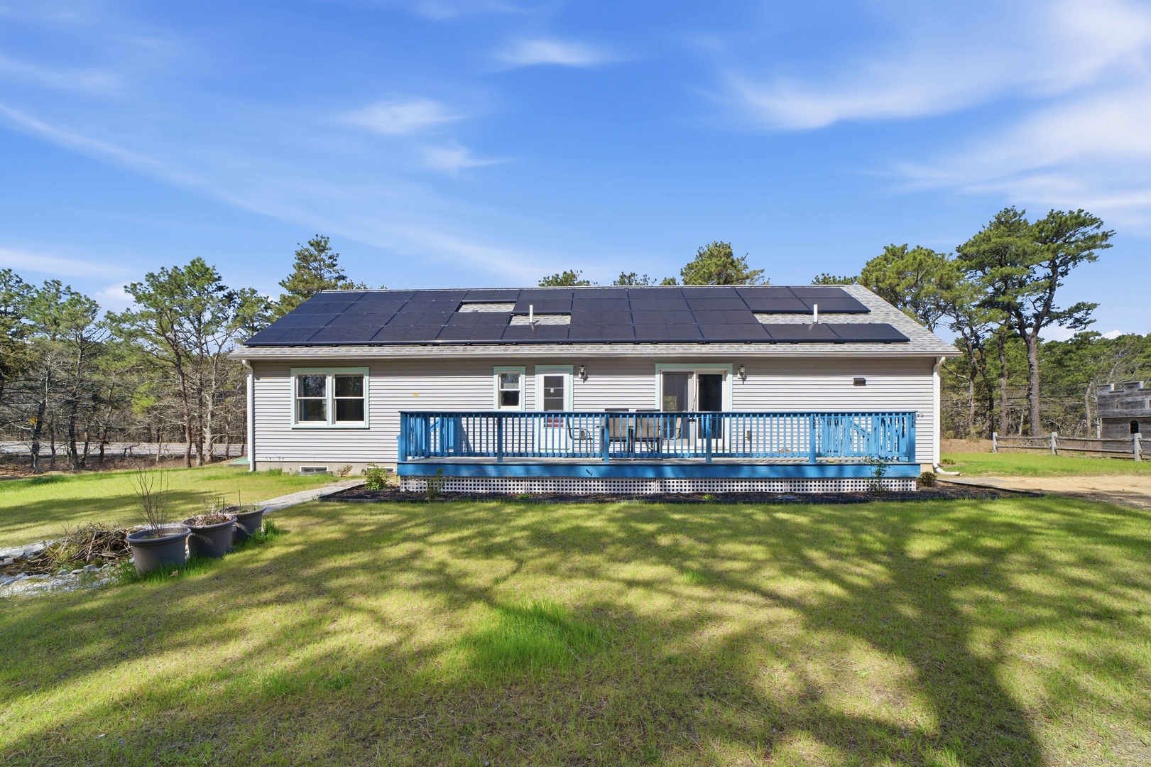 Eco-friendly ranch-style home featuring solar panels and a spacious blue deck surrounded by peaceful wooded grounds.
