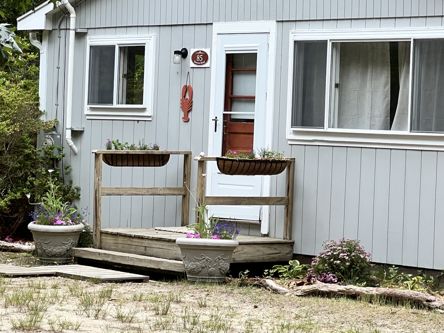 Charming cottage entrance with garden planters and coastal details welcomes you to a peaceful retreat.