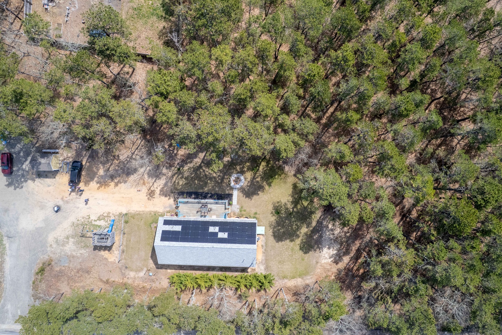 Aerial view of a secluded property nestled among mature trees, offering privacy and natural surroundings with solar panels and ample parking space.