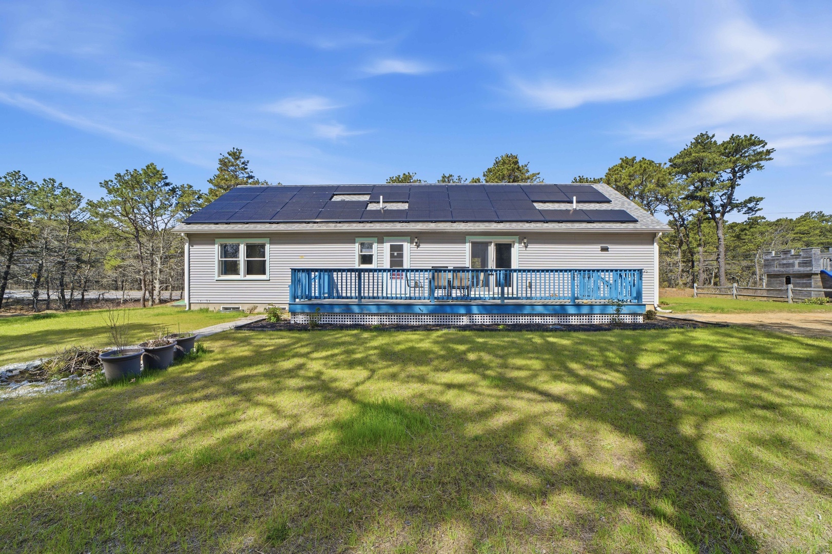 A modern vacation home featuring solar panels and a spacious blue deck surrounded by peaceful wooded grounds.