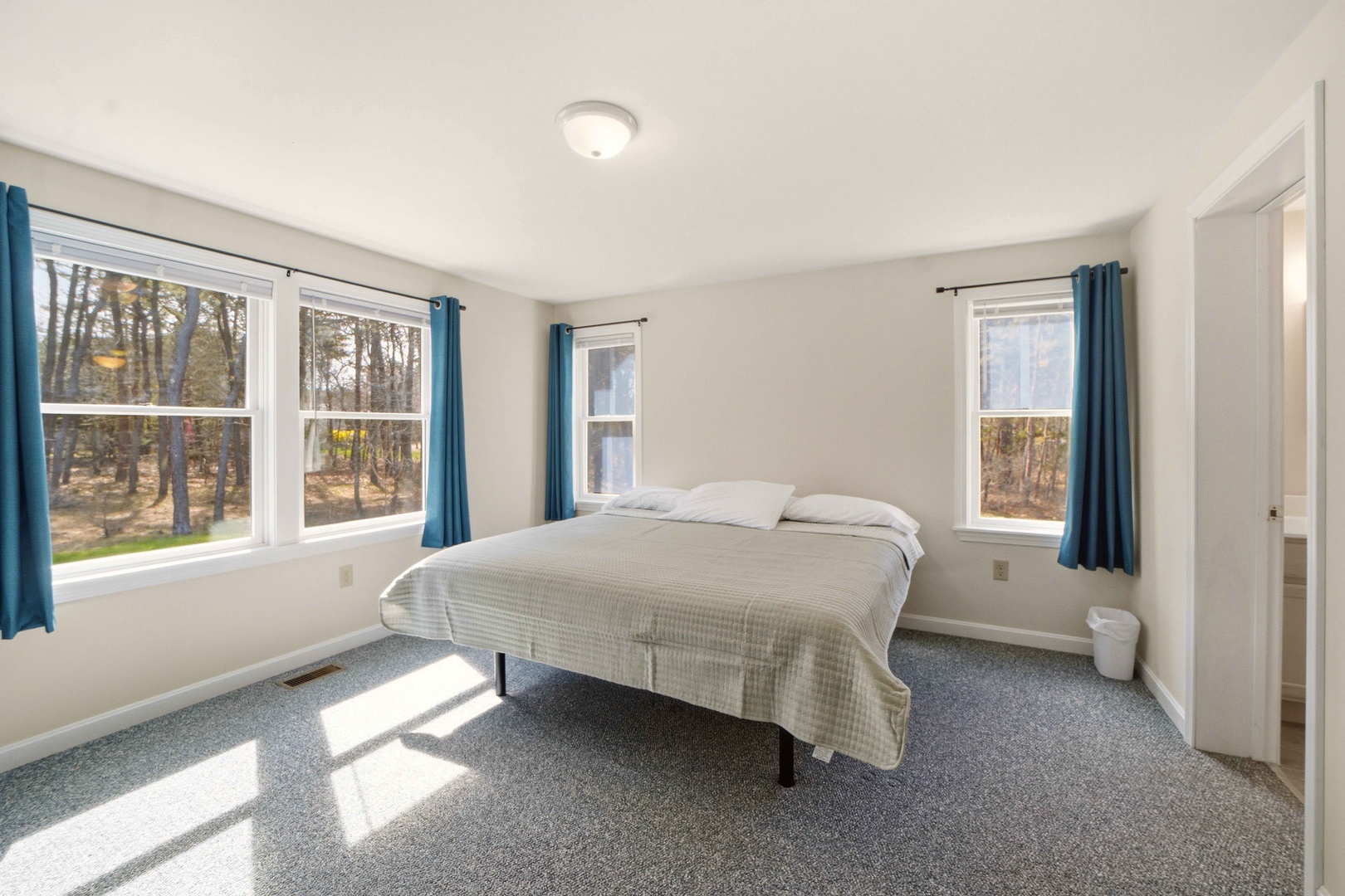 Rest peacefully in your bright bedroom with forest views streaming through multiple windows and soft natural light.